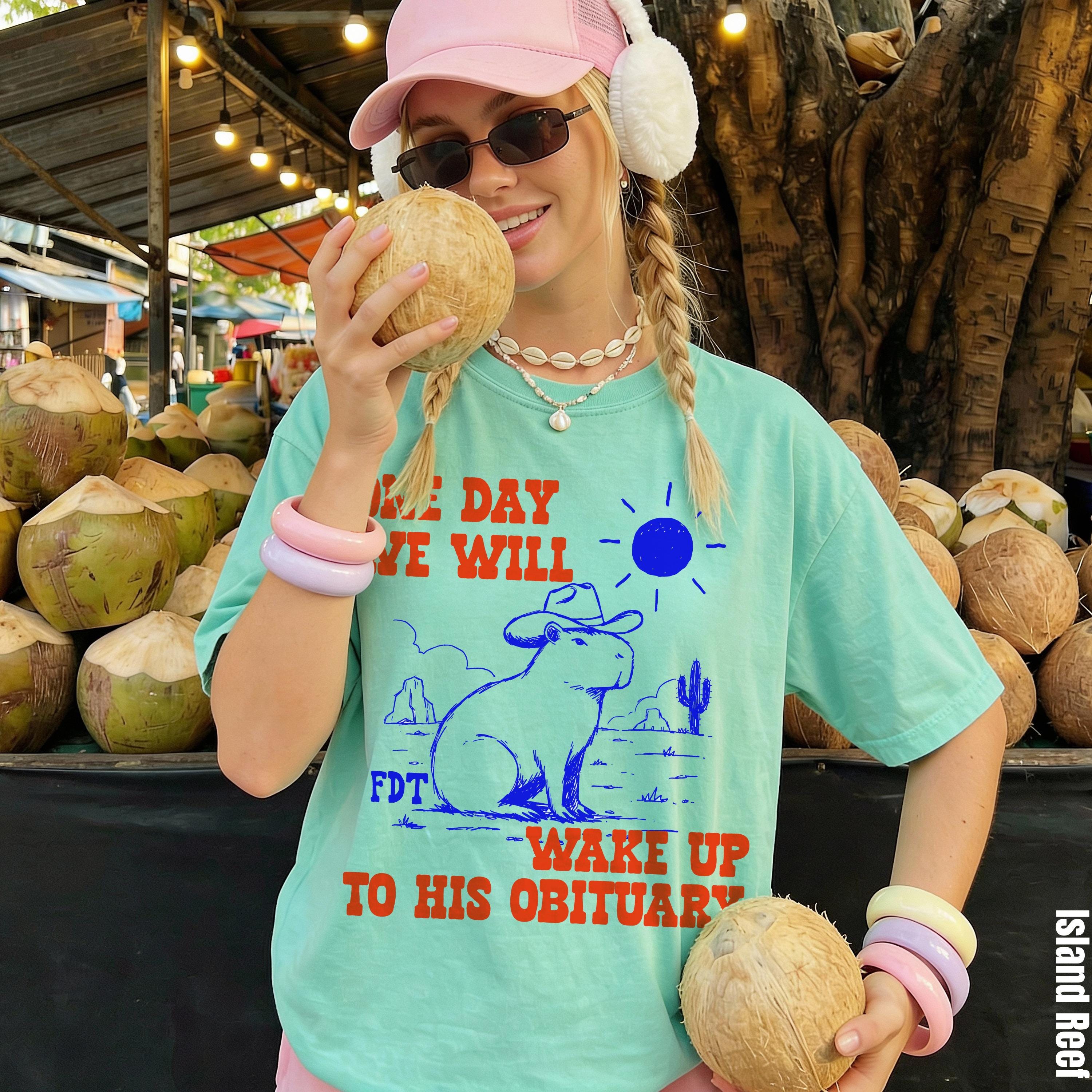 Mint t-shirt with a capybara in a cowboy hat and desert graphic, text reads "one day we will wake up to his obituary".