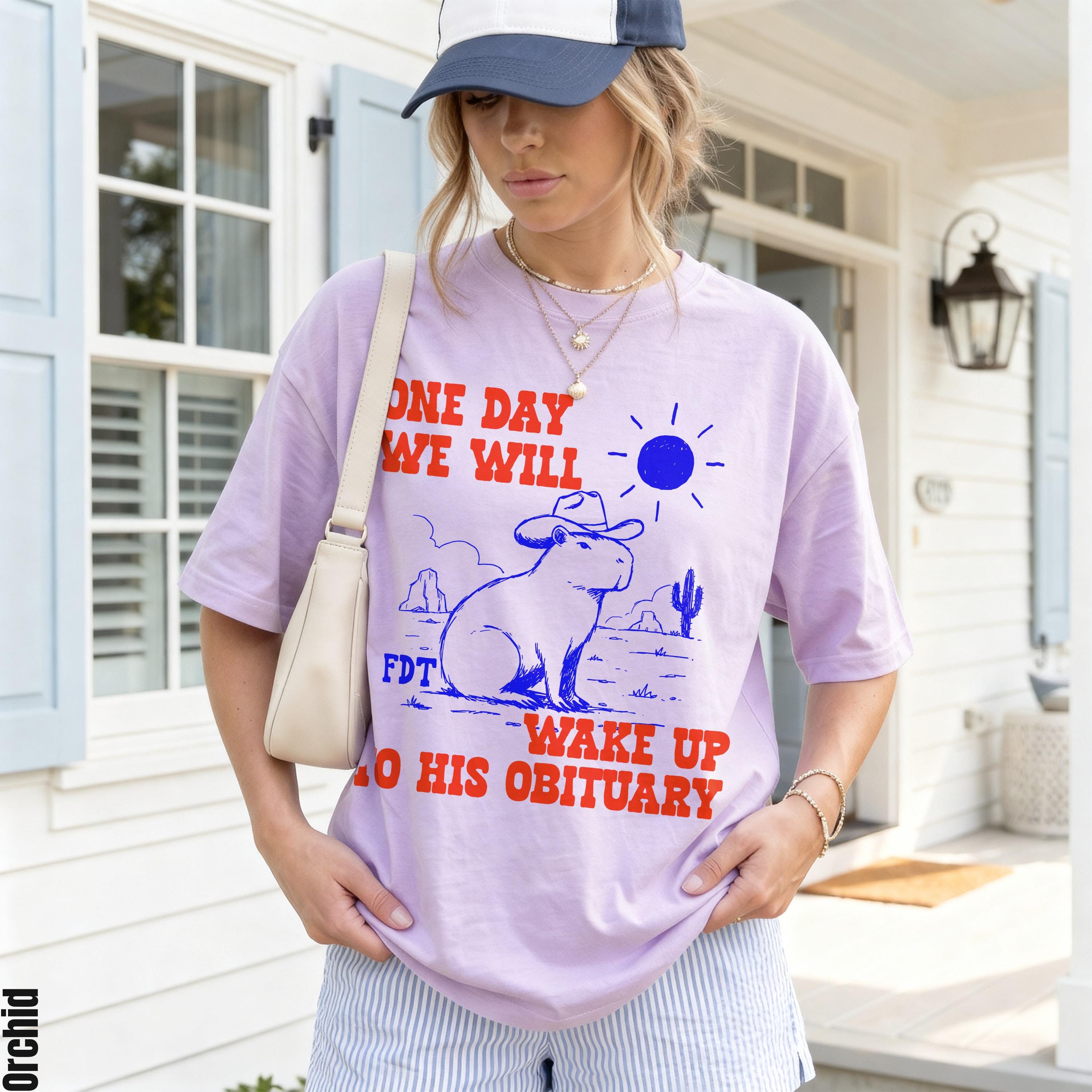 Light purple t-shirt with red text and blue graphic of a capybara in a desert.