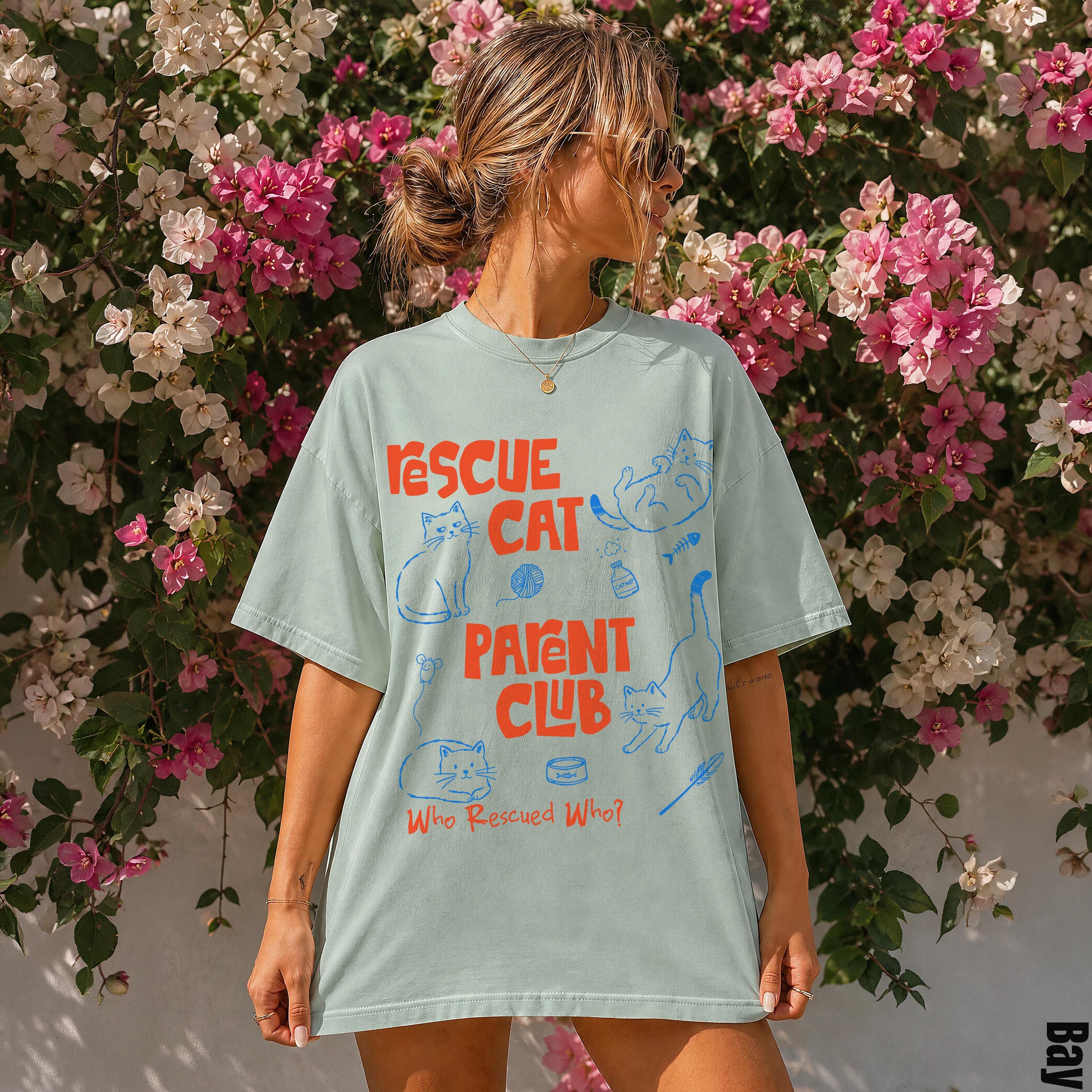 Light blue t-shirt with cartoon cats and "Rescue Cat Who Rescued Who?" text.