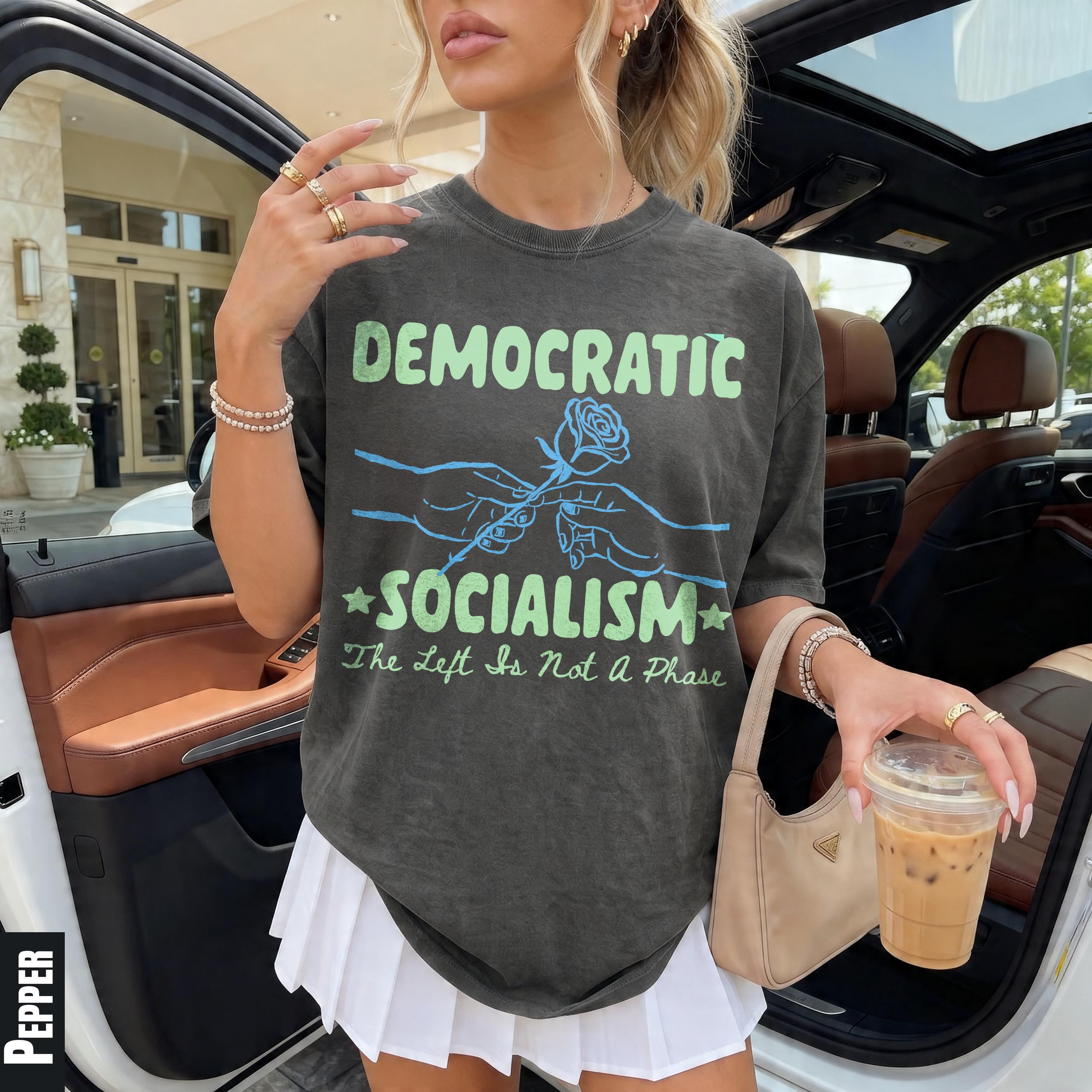 Woman wearing grey t-shirt with "Democratic Socialism" graphic, holding iced coffee.