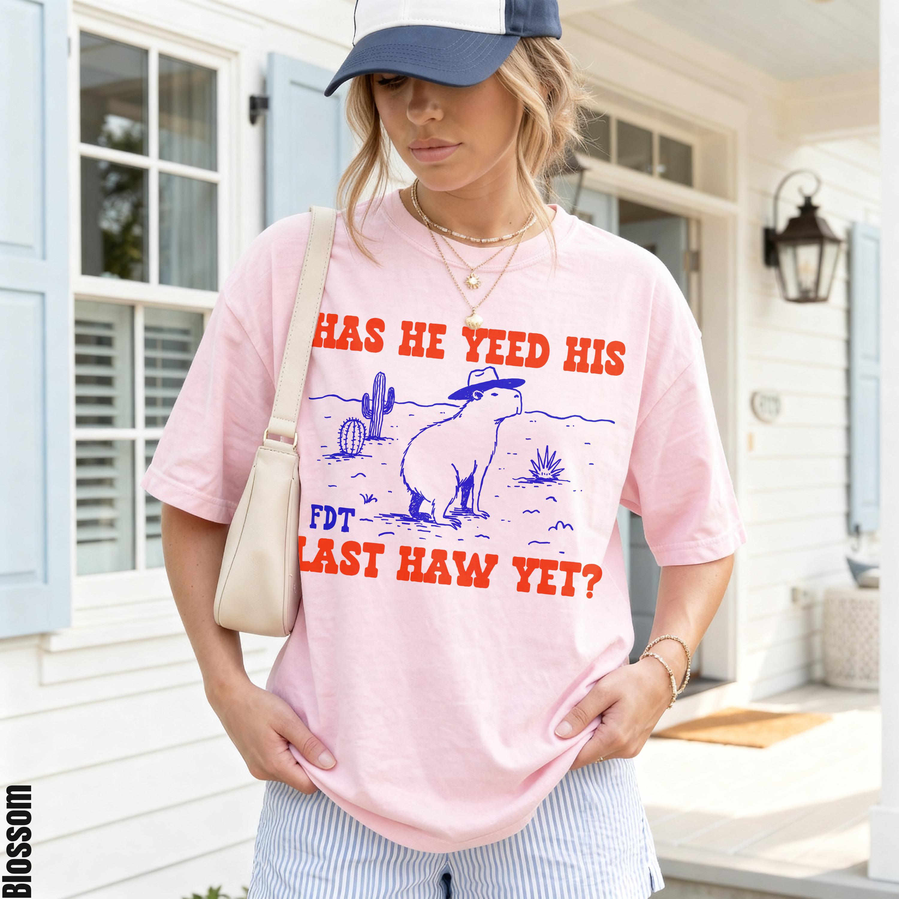 Pink t-shirt with cartoon capybara in hat and text "HAS HE YEED HIS LAST HAW YET?".