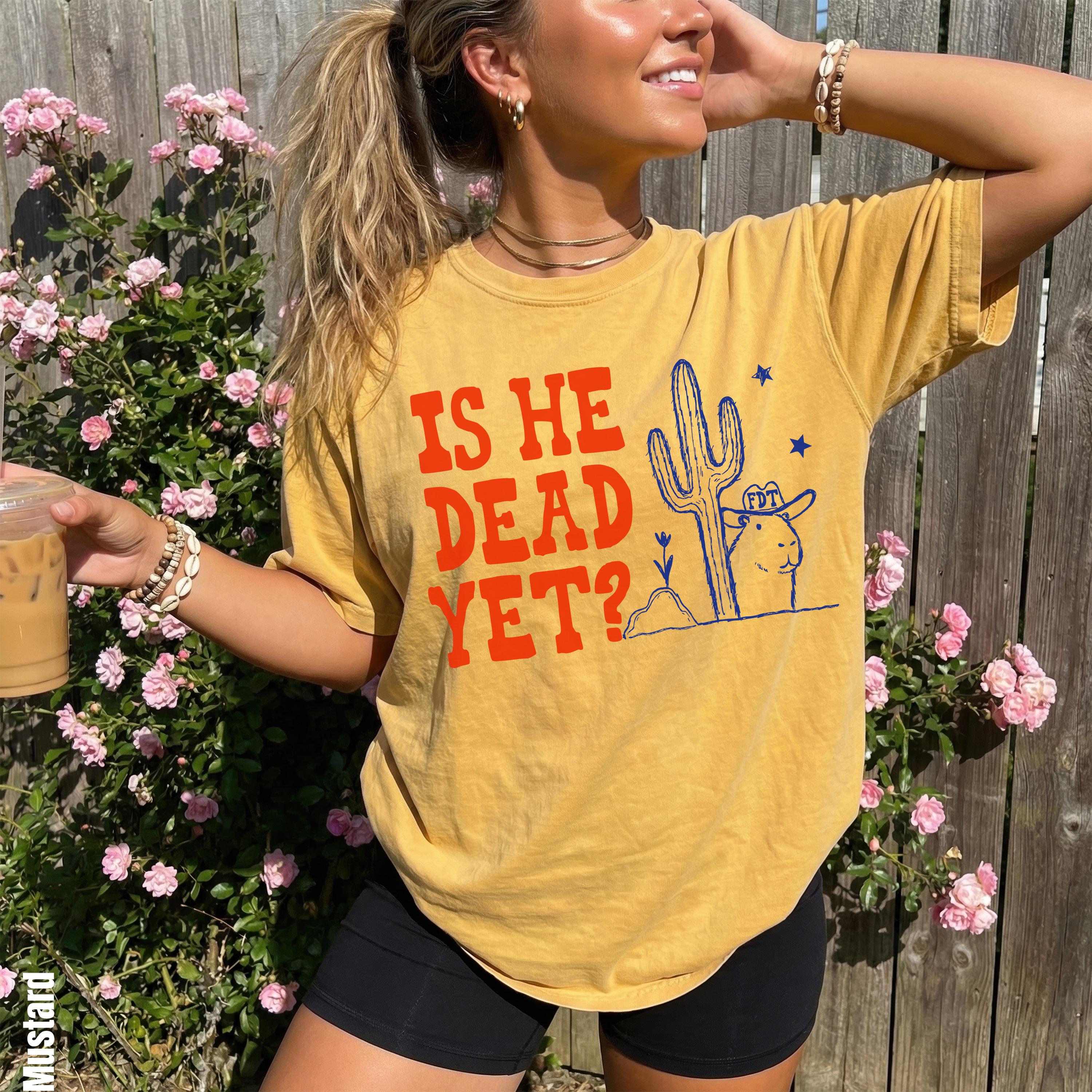 Yellow t-shirt with distressed graphic of cactus, llama, and text "IS HE DEAD YET?".