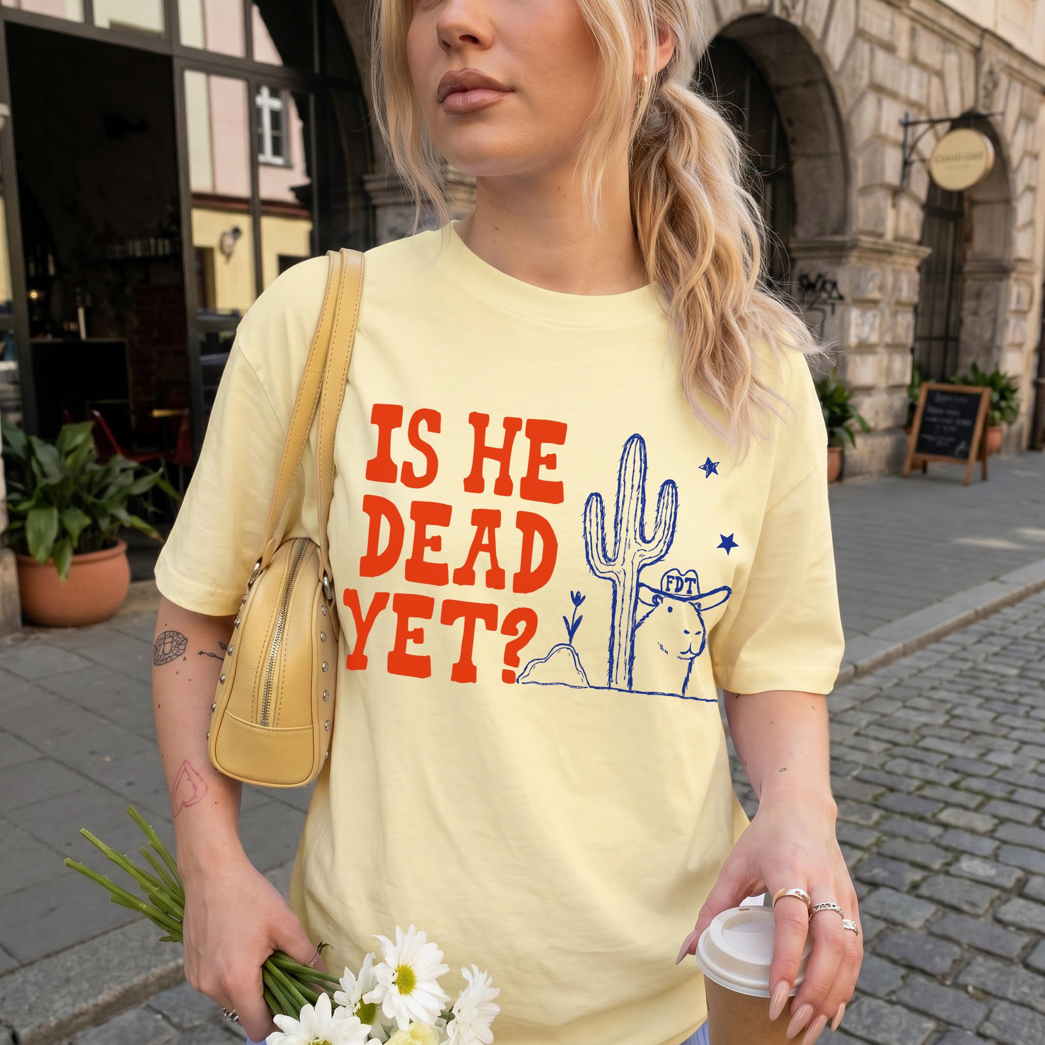 Light yellow t-shirt with red text "IS HE DEAD YET?" and blue desert graphic.