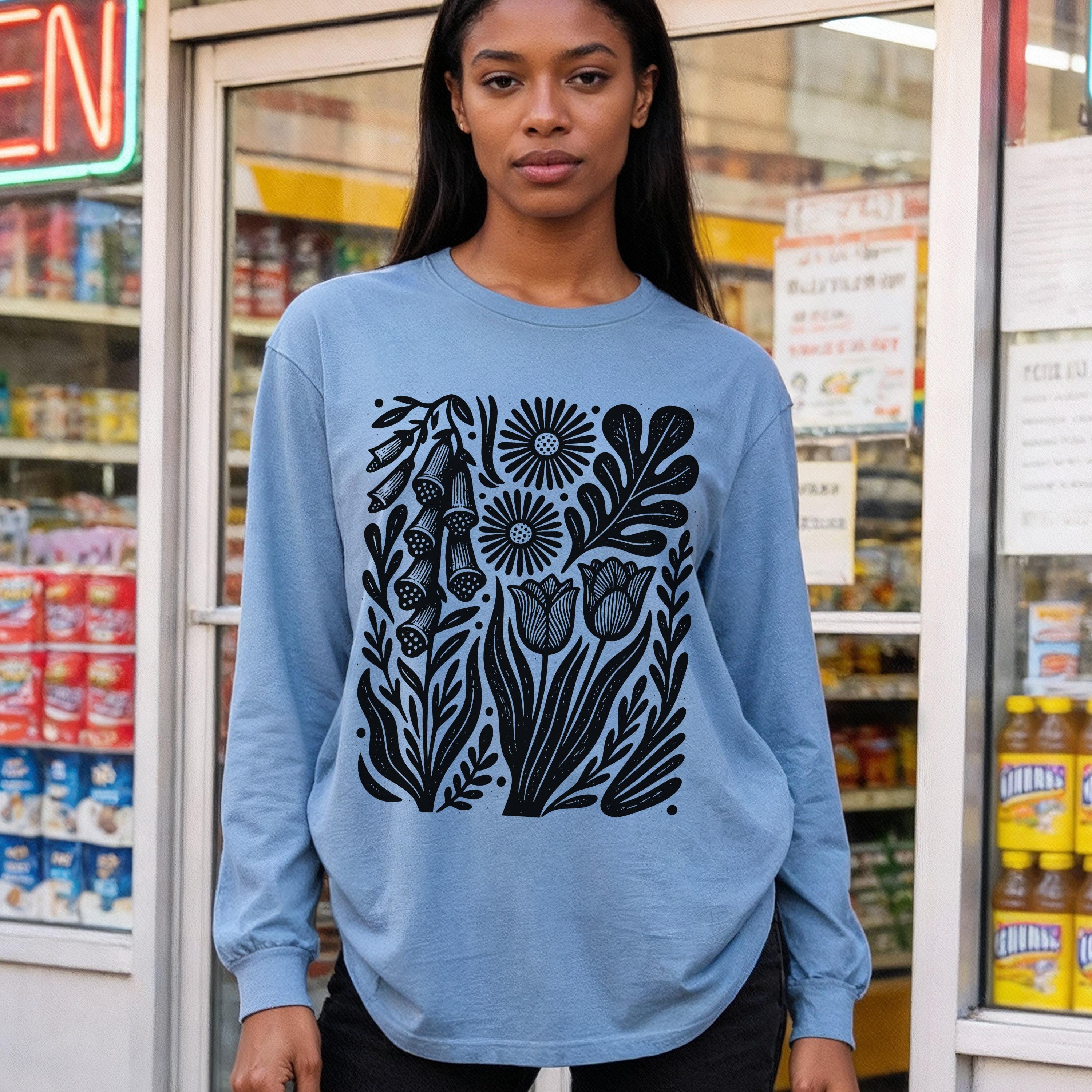 Blue long-sleeve shirt with black graphic of flowers and leaves.