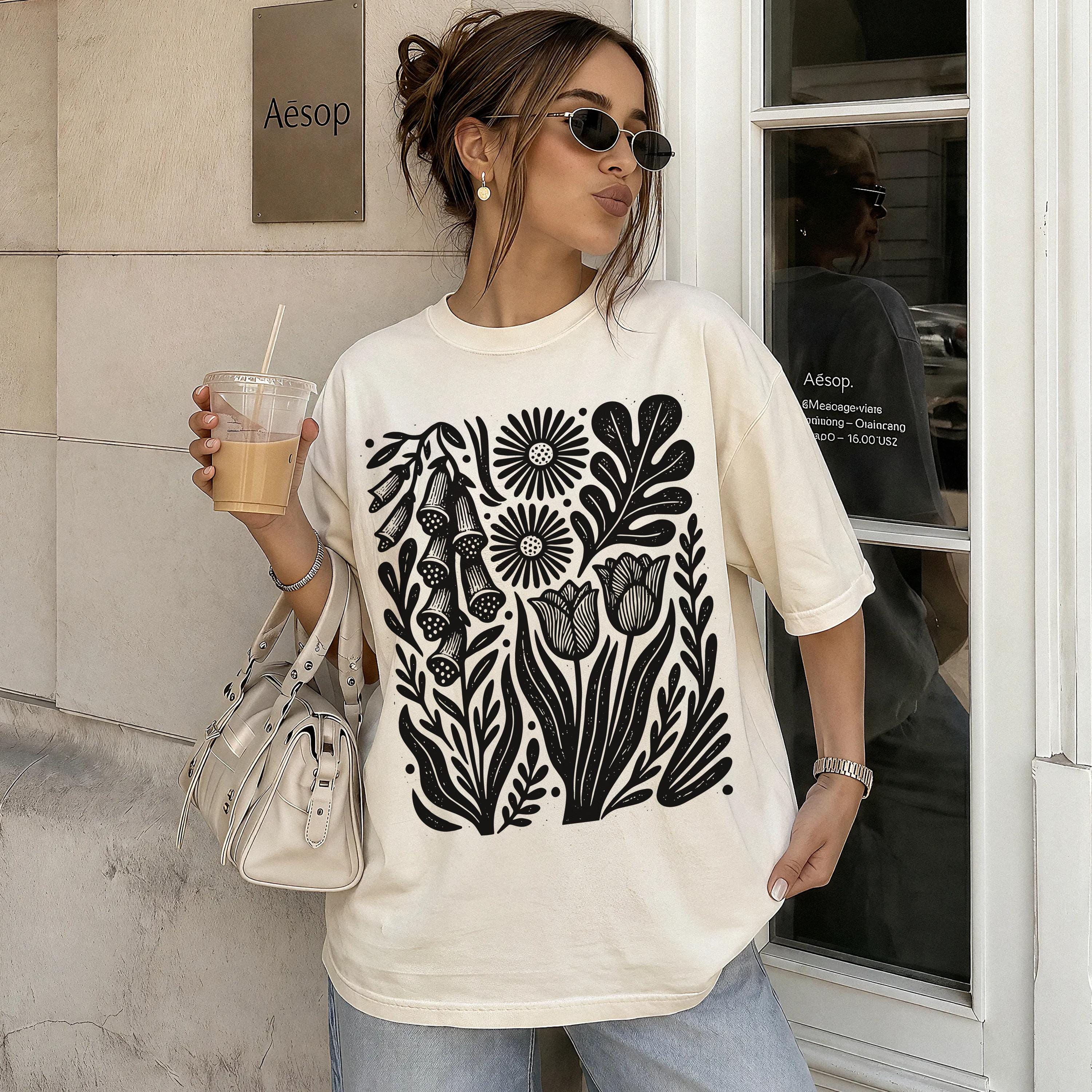 Cream t-shirt with black floral print, worn by a woman holding iced coffee.