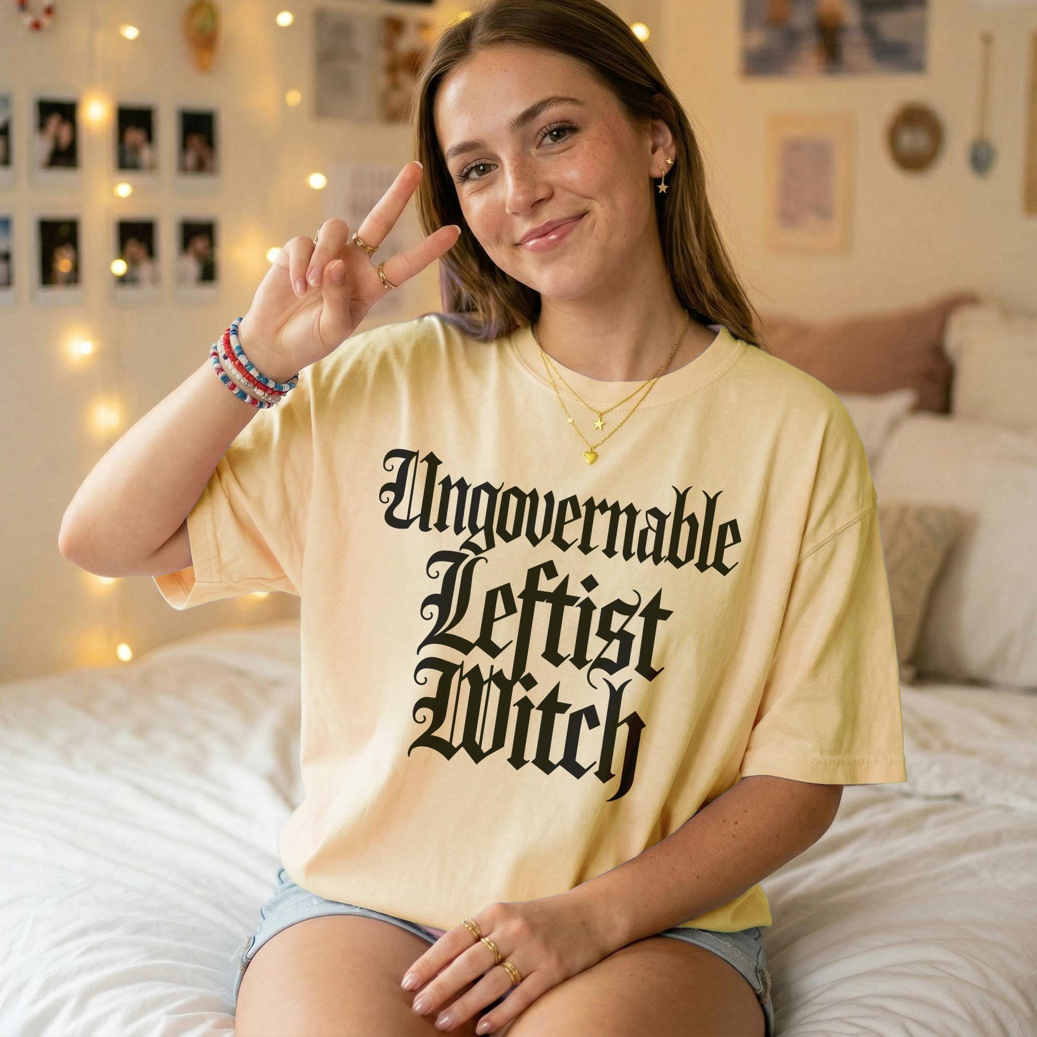 Young woman in a pale yellow t-shirt with black gothic text reading "Ungovernable Leftist Witch".