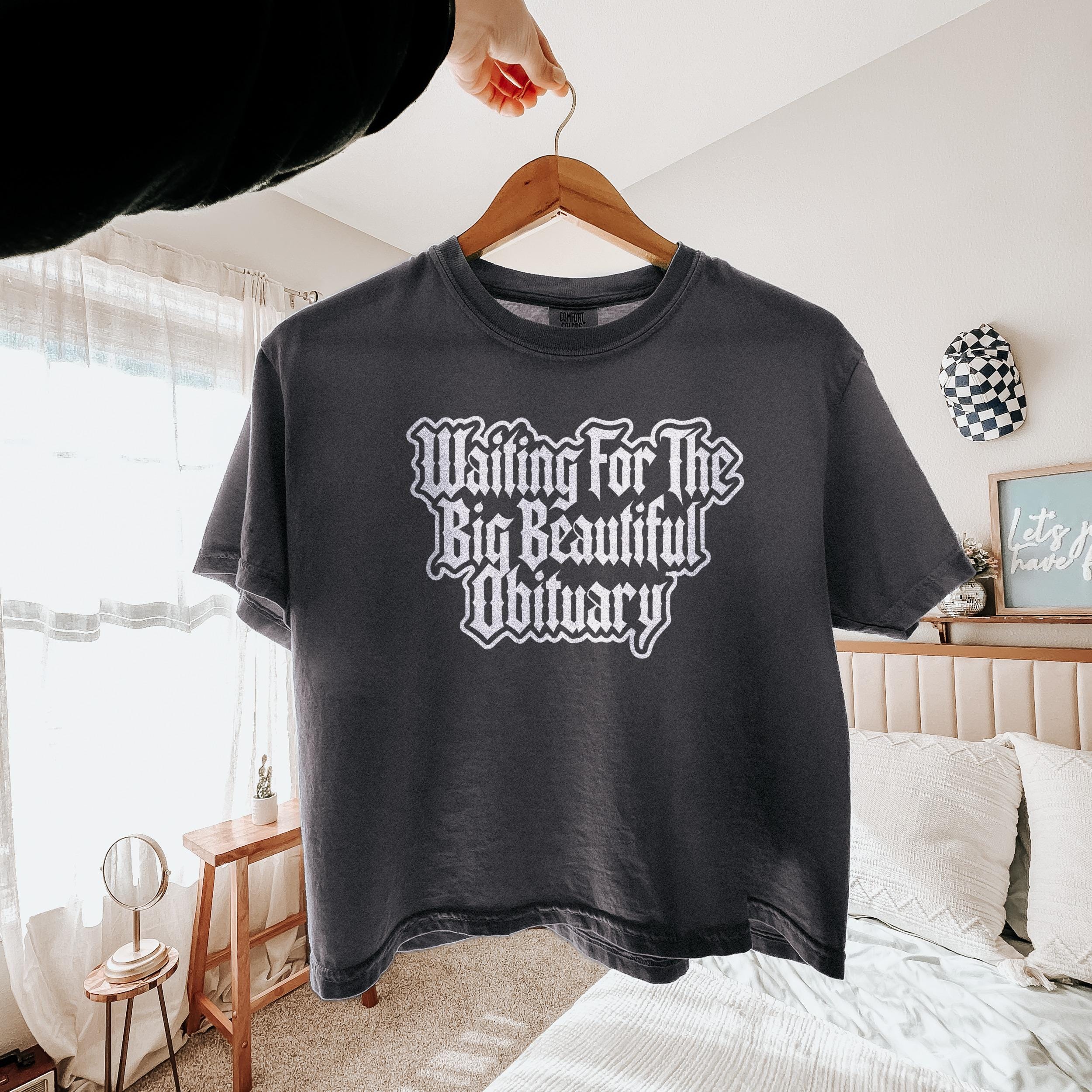 Dark gray t-shirt with "Waiting For The Big Beautiful Obituary" text.