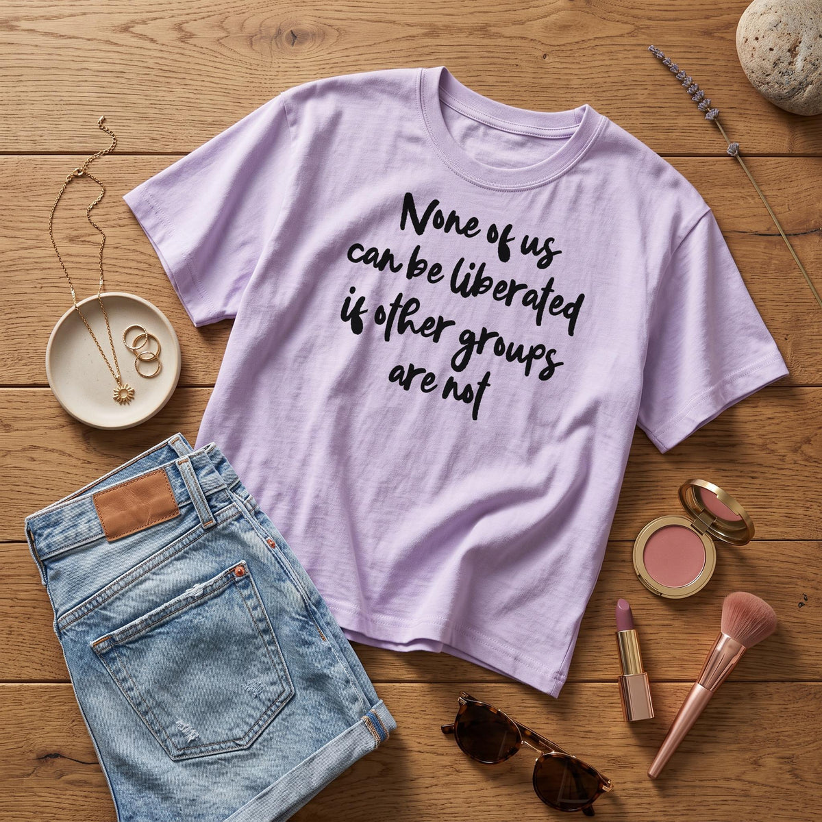 Lavender t-shirt with black text "None of us can be liberated if other groups are not."