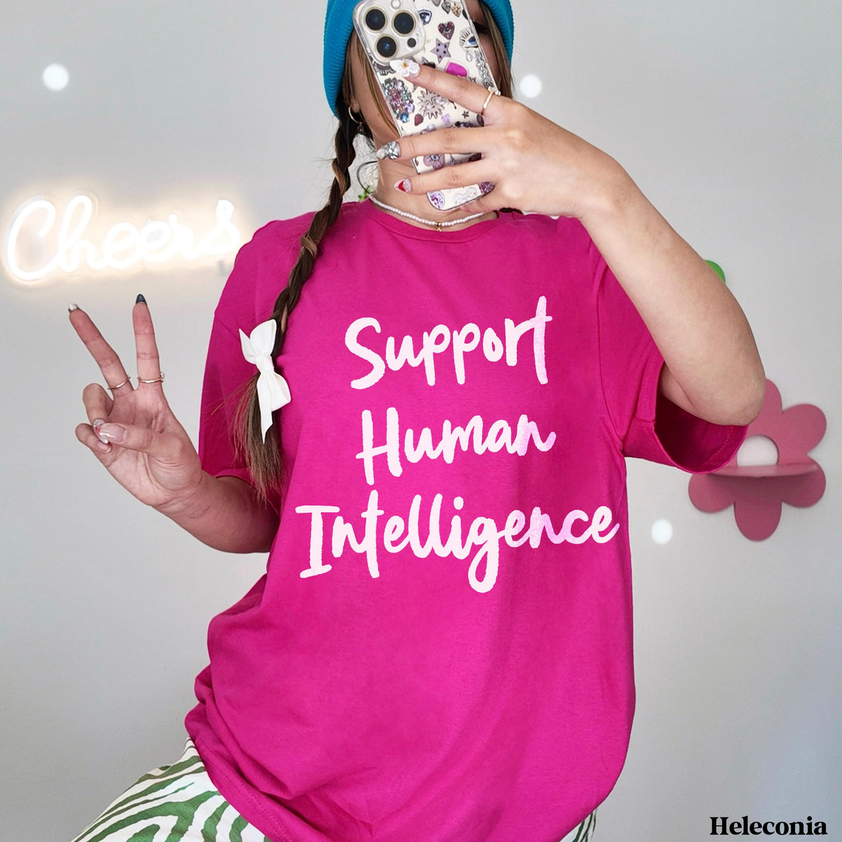 Pink t-shirt with "Support Human Intelligence" text, worn by a person holding a phone.