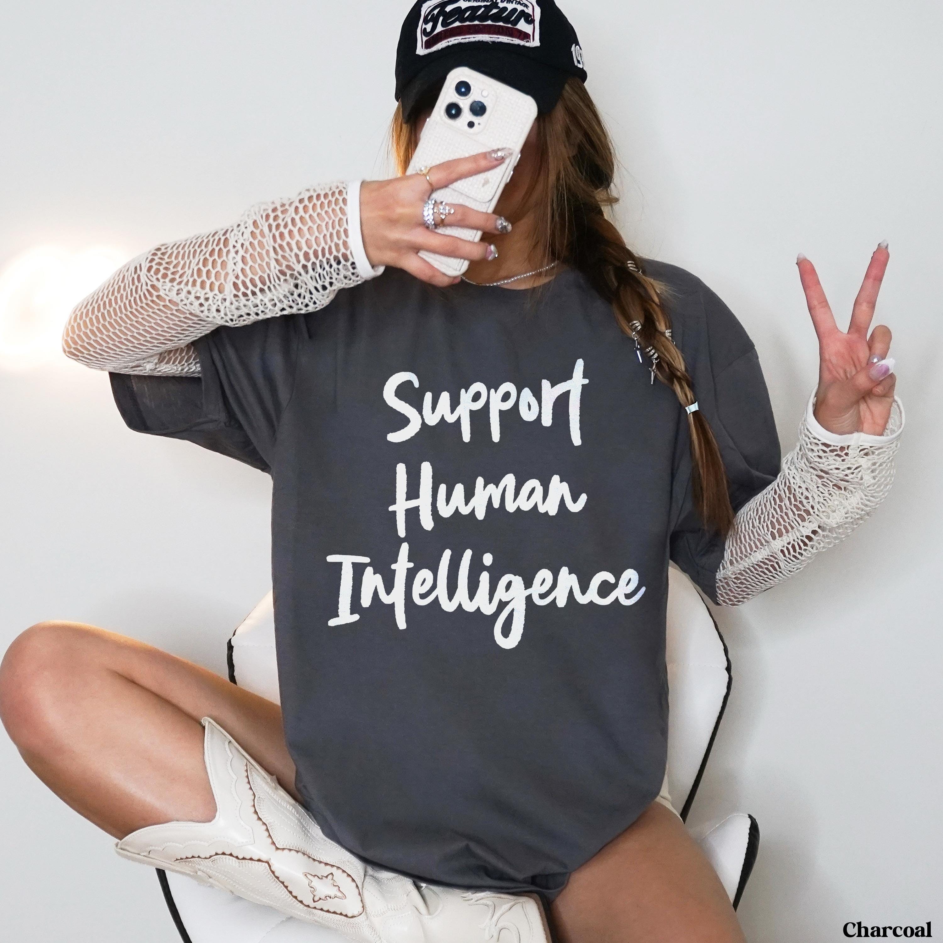Charcoal t-shirt with "Support Human Intelligence" text, worn by a woman holding a phone and making peace sign.