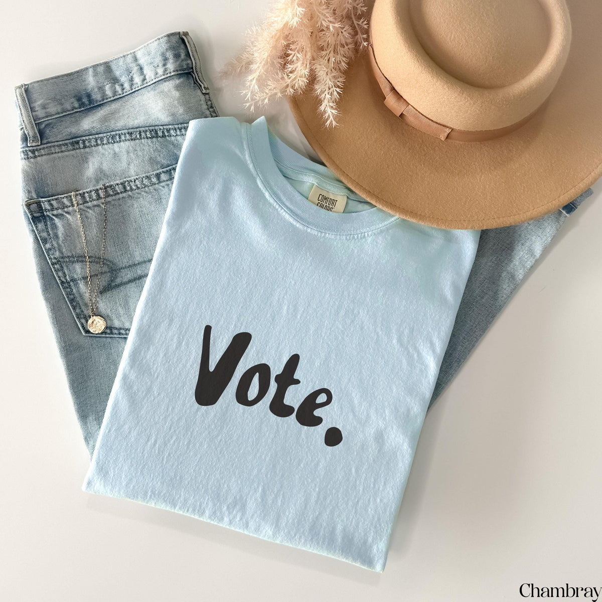 Light blue t-shirt with "Vote." text, jeans, hat, and necklace.