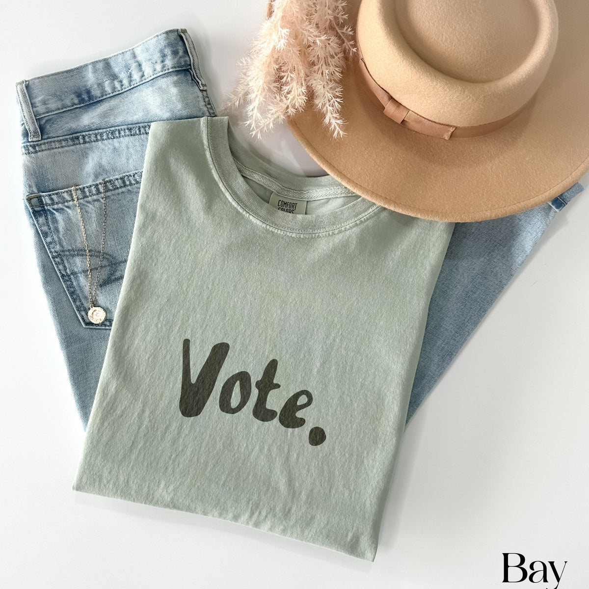 Light green t-shirt with "Vote." text, jeans, hat, and necklace.