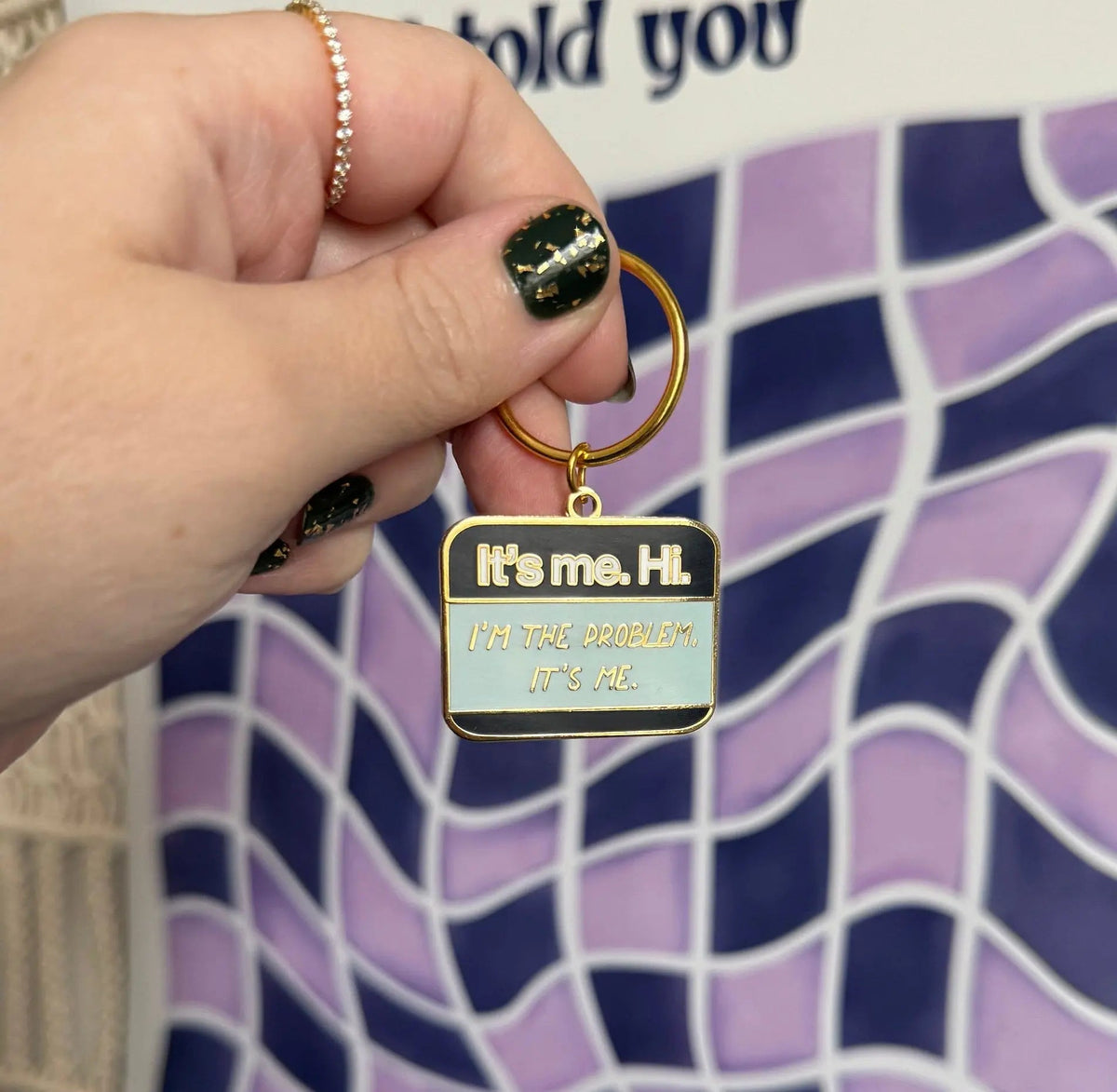 It’s me Hi I’m the problem It’s me enamel keychain detail — close up of the gold hand lettering on navy enamel by indie artist MangoIllustrated