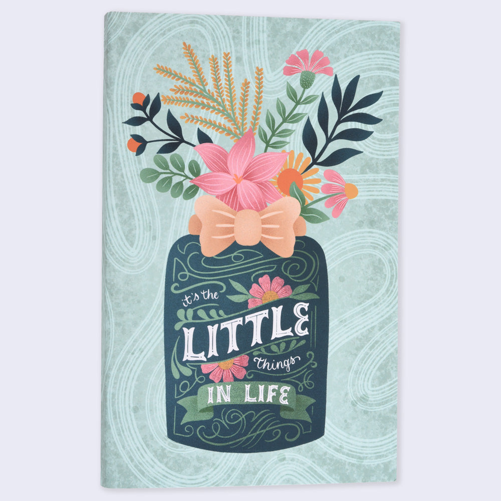 A flat lay notebook with a colorful cover featuring a botanical design and a textual phrase &