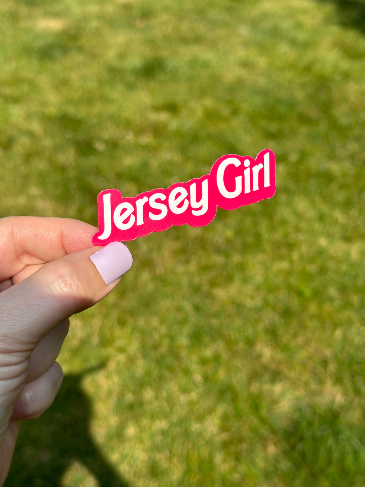 A hand holding a pink sticker with the text &