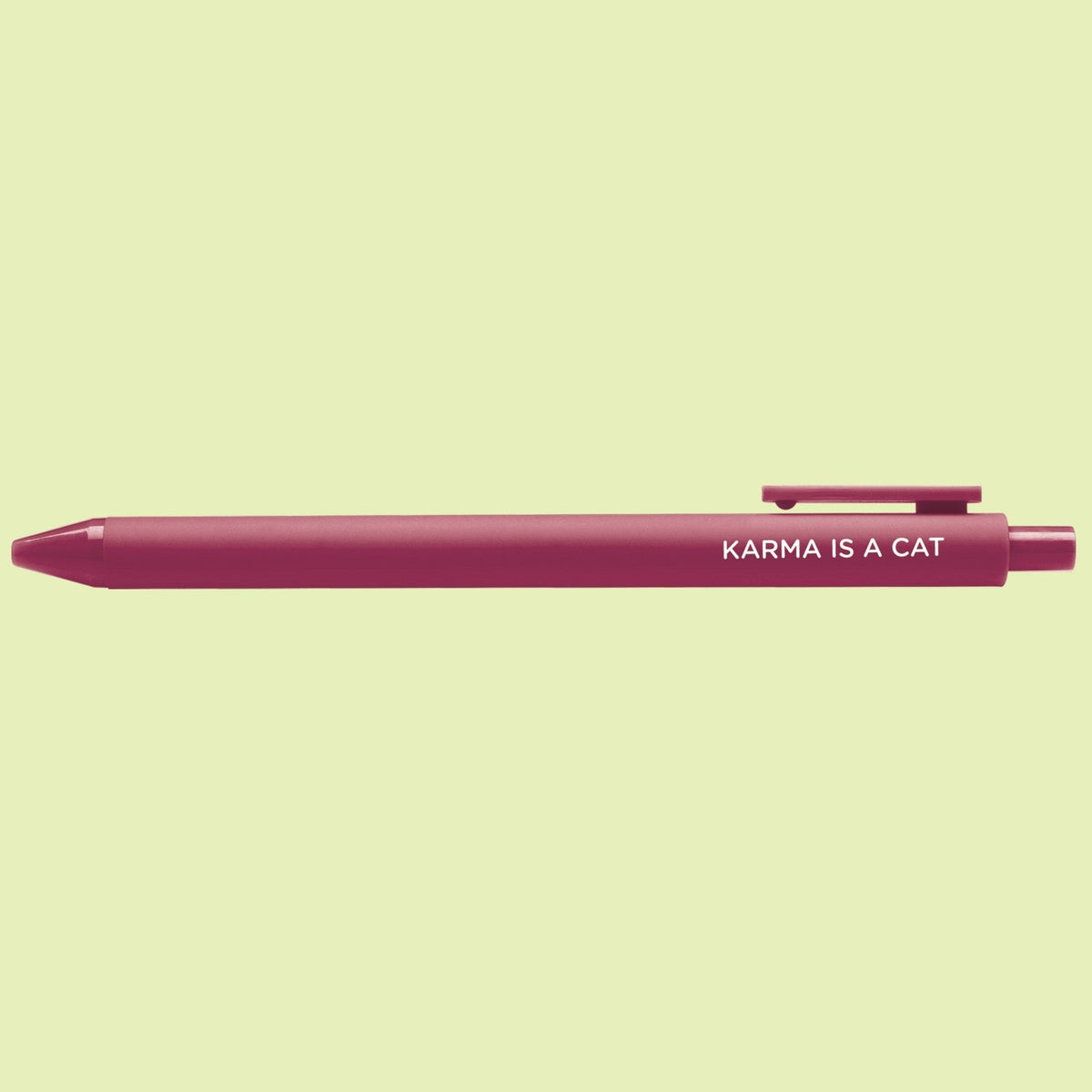 Karma is a Cat pen flat lay — maroon jotter gel pen on a light green background by indie artist MangoIllustrated