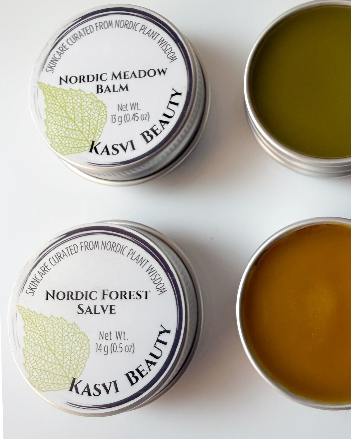Kasvi Beauty Nordic Meadow Balm and Nordic Forest Salve. Two metal tins with lids open to expose the balm green color and golden color of the salve.