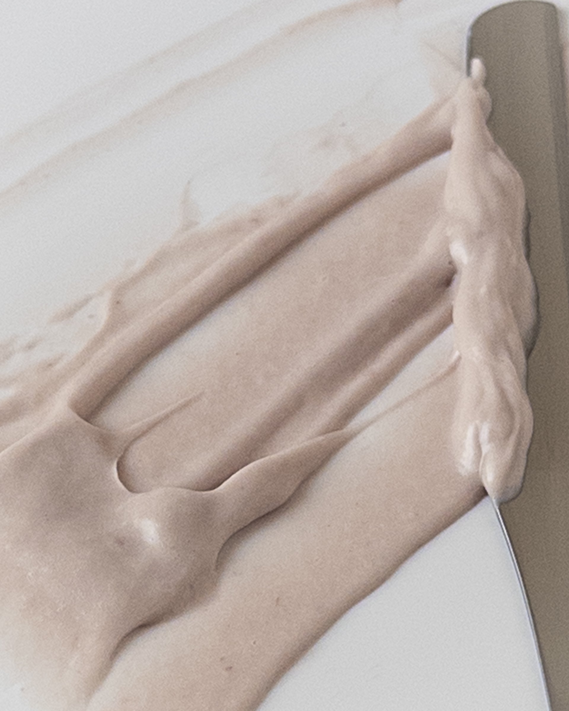 Close-up of color pale purple and cream texture of Bilberry Dream Cream face moisturizer spread with spatula against white background.