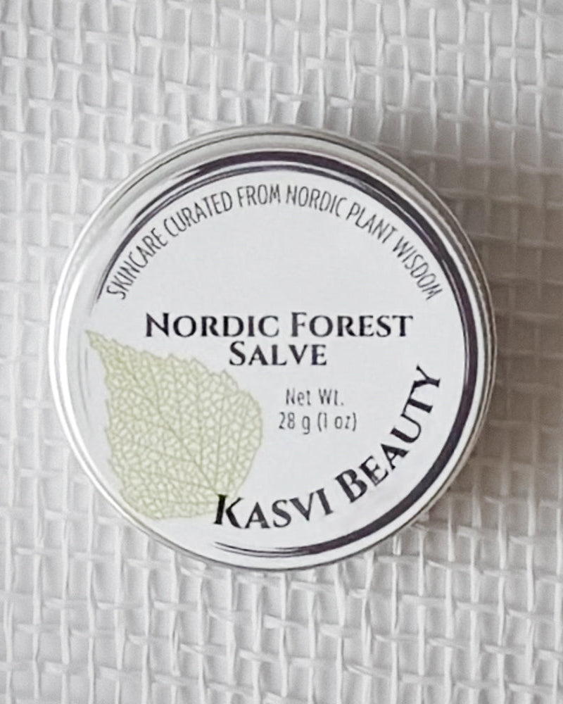 A round silver tin of Kasvi Beauty Nordic Forest Salve on a textured white woven background. The lid is white with black text and a light green birch leaf illustration.
