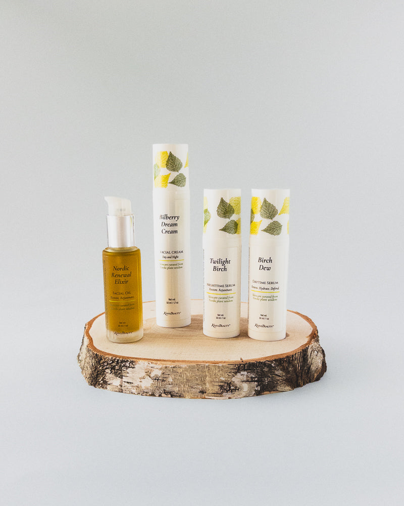 Four skincare products from Kasvi Beauty Birch Collection arranged on a rustic wood slice pedestal against a light gray background. The set includes a &