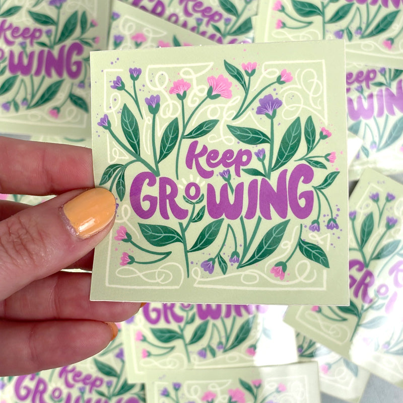 hand holding A sticker with a floral design and the text &