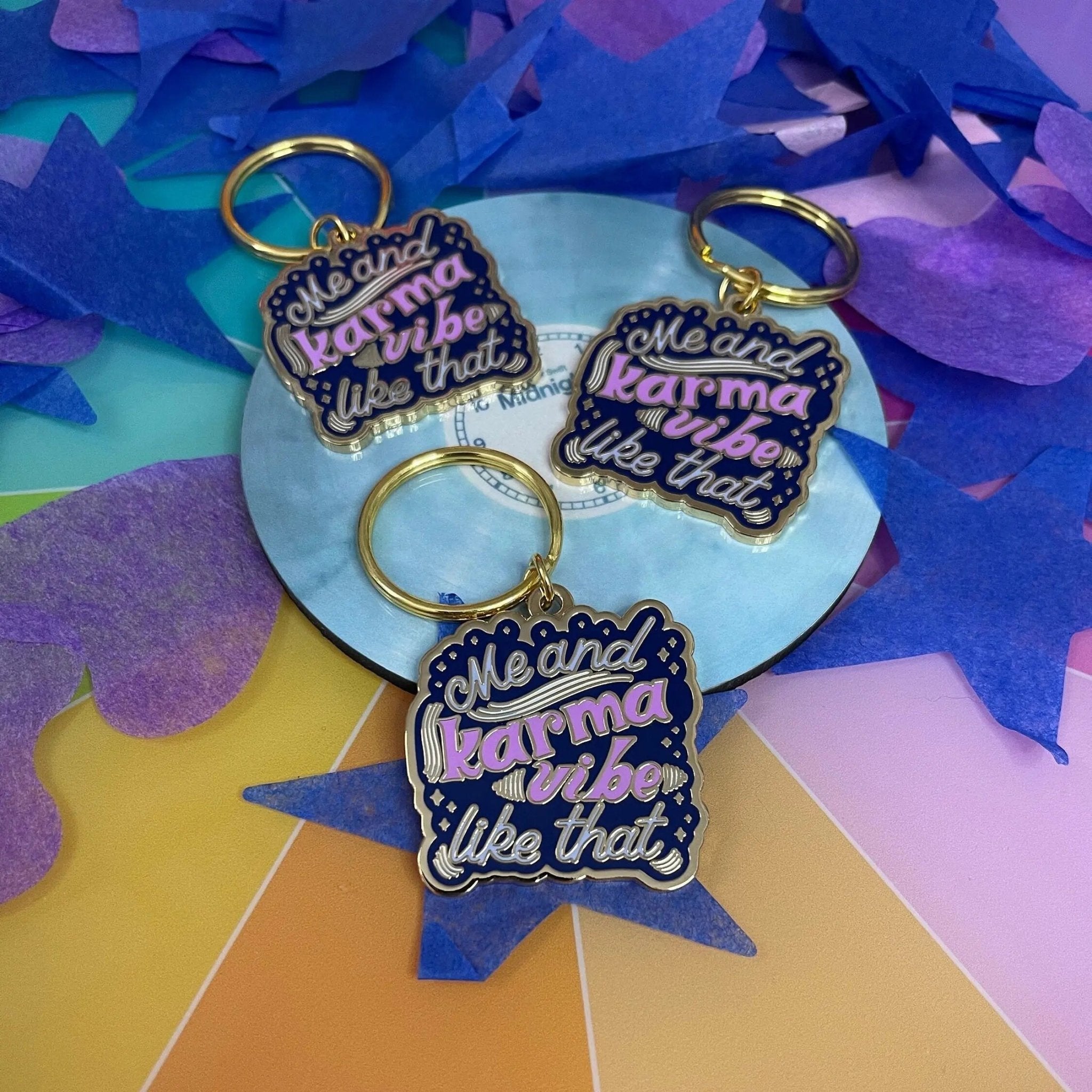 Me and Karma Vibe Like That enamel keychain angled view — gold metal edge and navy enamel bag charm by indie artist MangoIllustrated