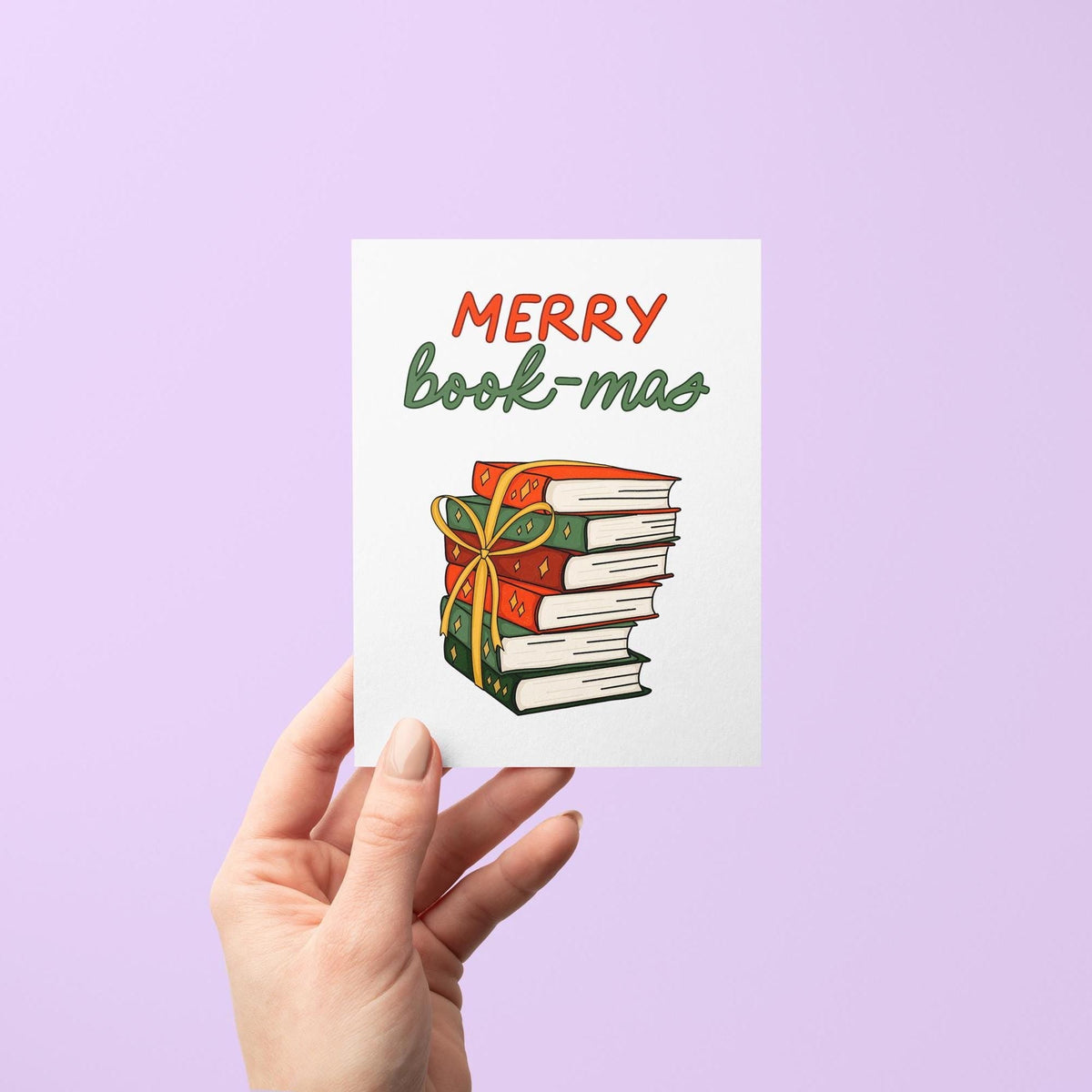Merry Book-mas card flat lay — bookish Christmas card styled with a stack of books, by indie artist MangoIllustrated