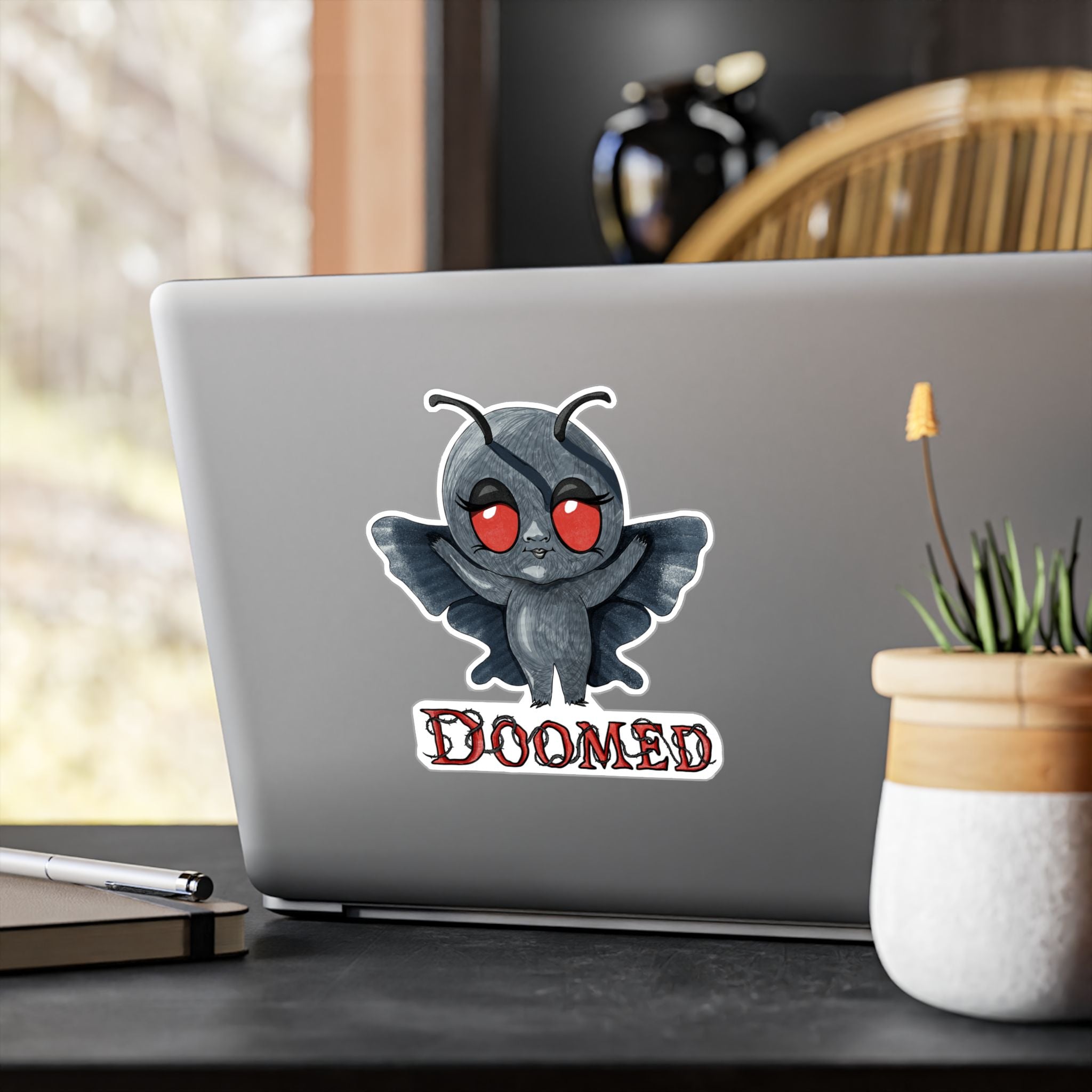 Large Mothman cryptid sticker on the back of a silver laptop by a window
