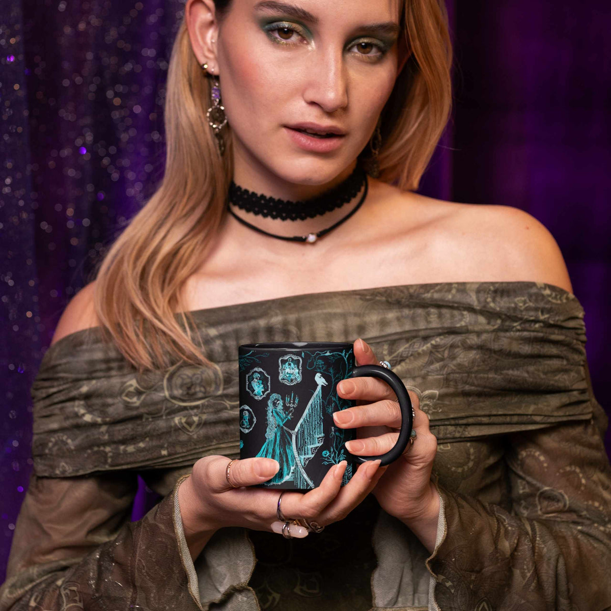 Woman in an olive off-shoulder top and black lace choker holding a teal zombie toile mug