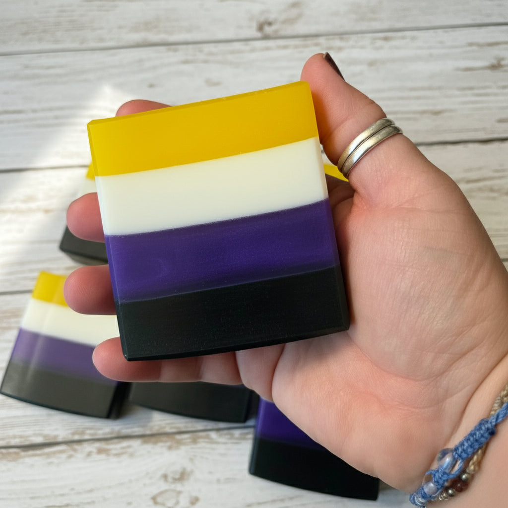 Hand holding a nonbinary flag striped soap bar with a wooden background