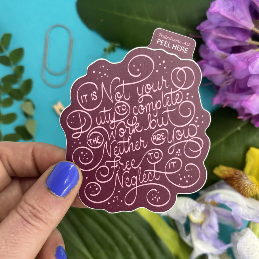 Decorative sticker with ornate lettering that reads "it is not your duty to complete the work but neither are you free to neglect it" held by a hand with blue nail polish
