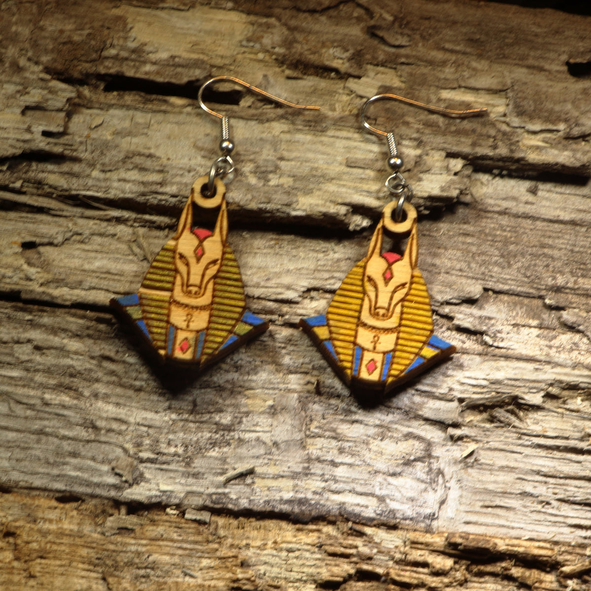 Hand-painted wooden Anubis dangle earrings featuring the jackal-headed Egyptian god with detailed ancient Egyptian artwork. Crafted from lightweight wood with hypoallergenic .925 sterling silver hooks, these mythological earrings are perfect for history lovers, Egyptology enthusiasts, mythology fans, museum gift shoppers, gothic fashion, and anyone who appreciates ancient civilization-inspired jewelry.