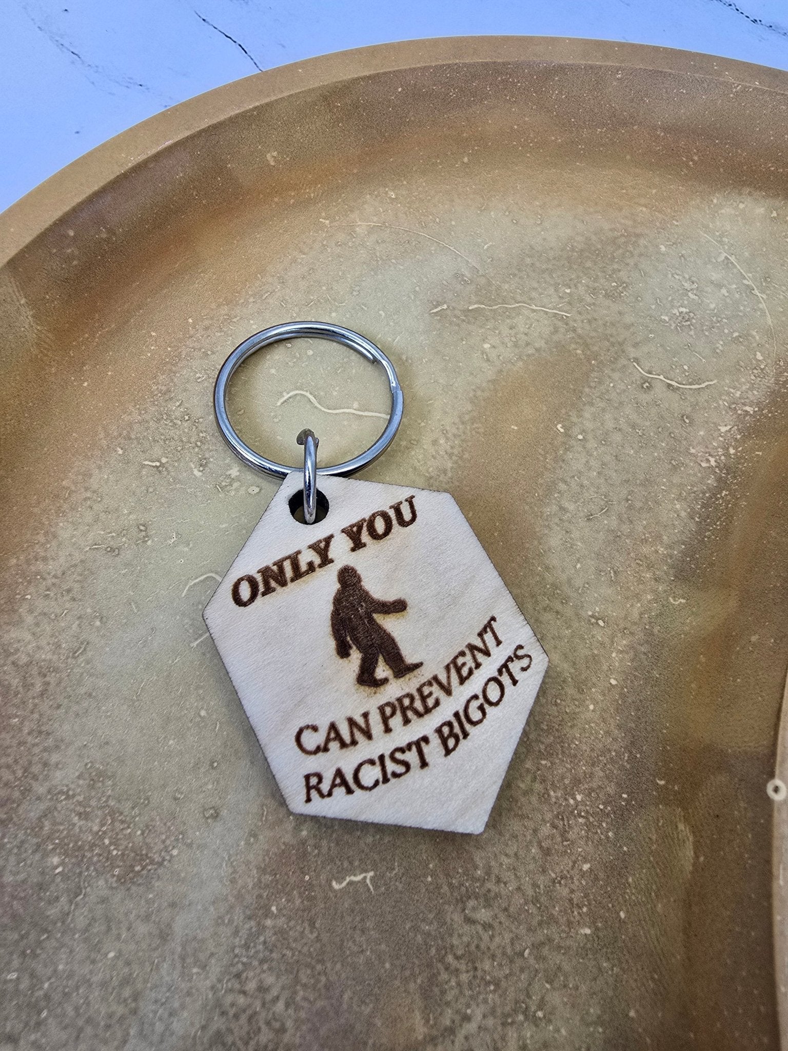 Birch wood keychain with laser-engraved Sasquatch silhouette and “Only You Can Prevent Racist Bigots” text, natural finish.