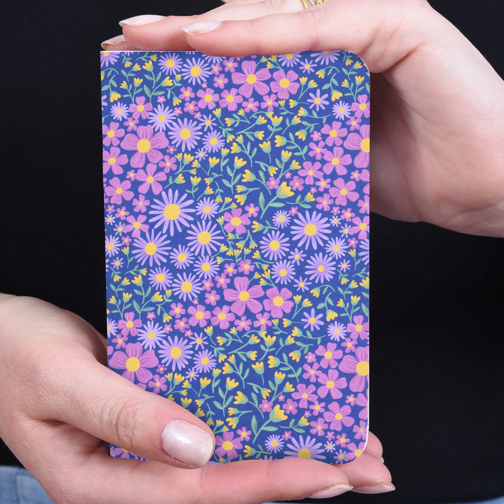 hands holding a small pocket notebook featuring a floral design on dark blue background