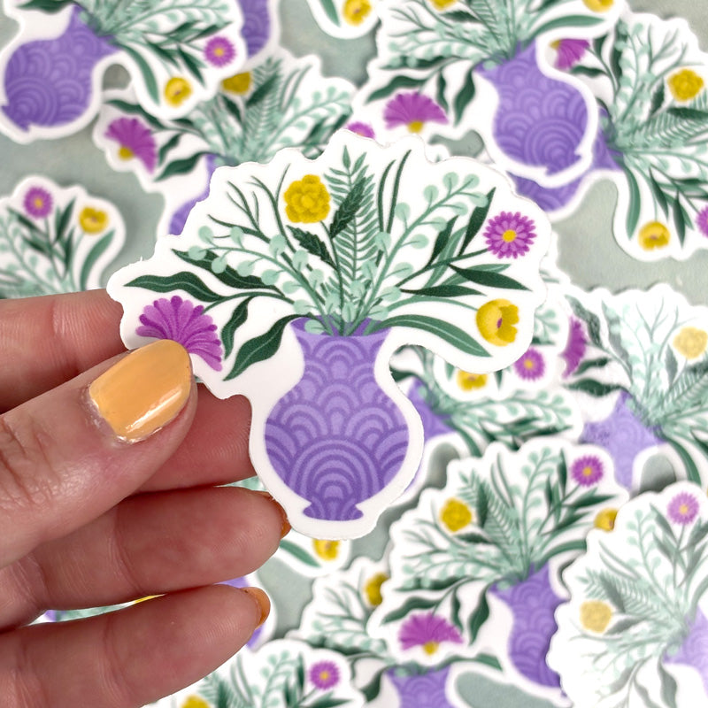 hand holding A sticker with a floral design featuring various colors like purple, green, and yellow, in a purple vase