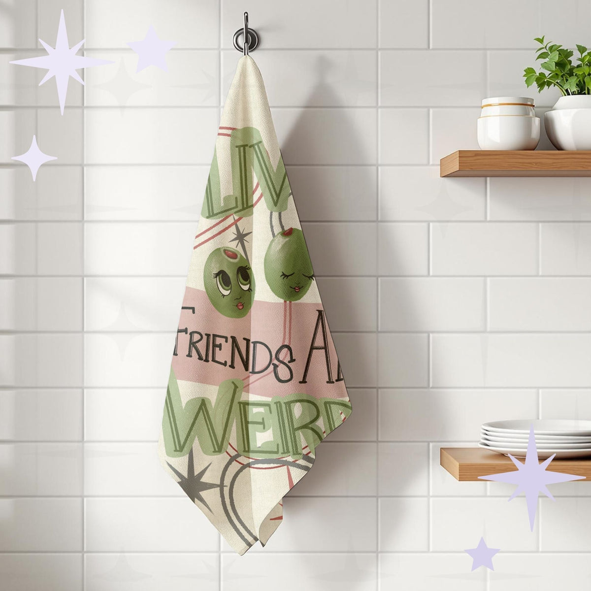 Funny retro olive tea towel hanging from a chrome kitchen hook against white subway tile, showing full illustrated design