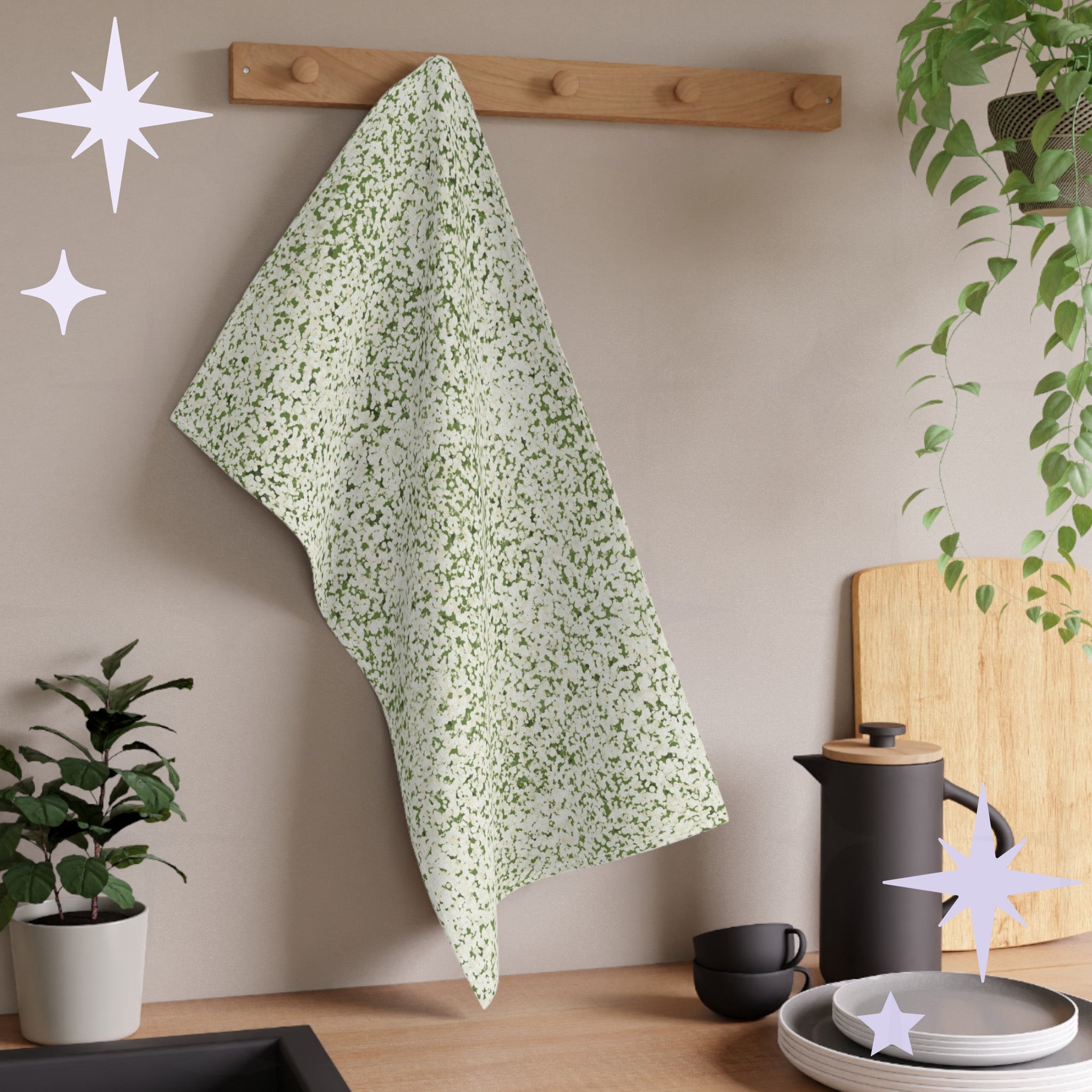 Sage green terrazzo kitchen towel hanging from wooden peg rail in neutral kitchen with houseplants, stacked plates, and matte black coffee equipment
