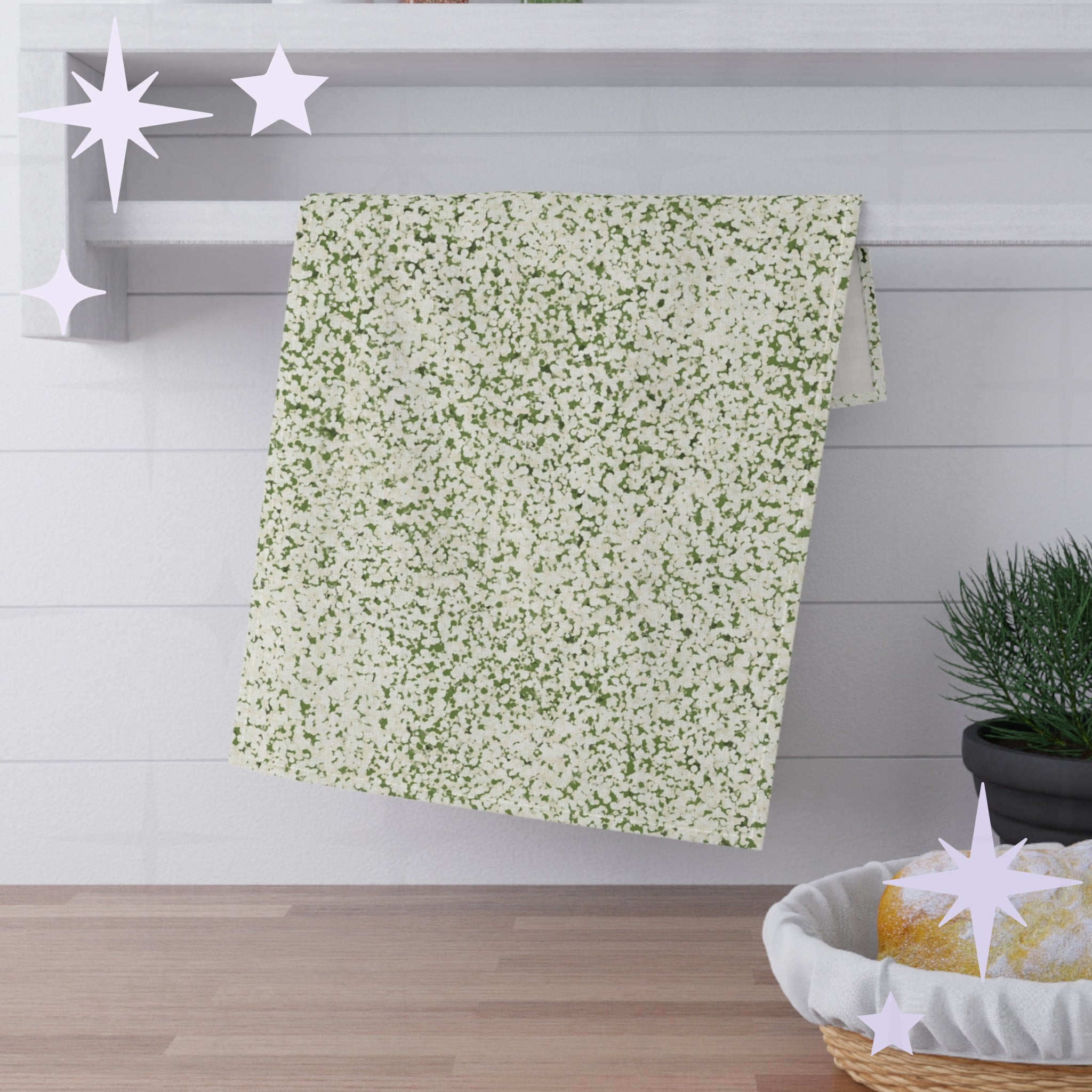 Sage green terrazzo tea towel folded and draped over white shaker shelf rail with pine plant and bread basket in background