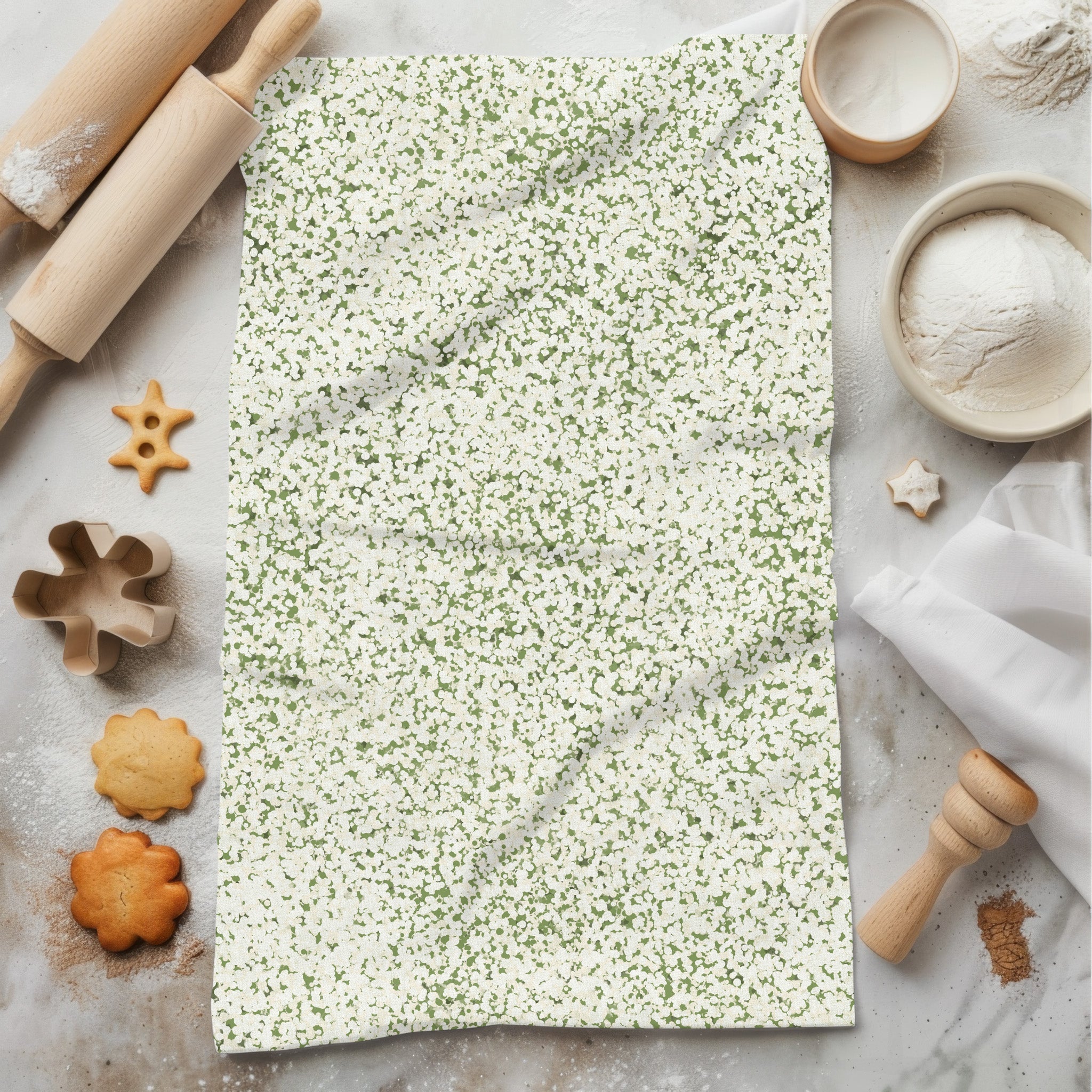Sage green terrazzo print tea towel laid flat on marble prep surface surrounded by baking props including rolling pin, cookie cutters, flour and shaped cookies