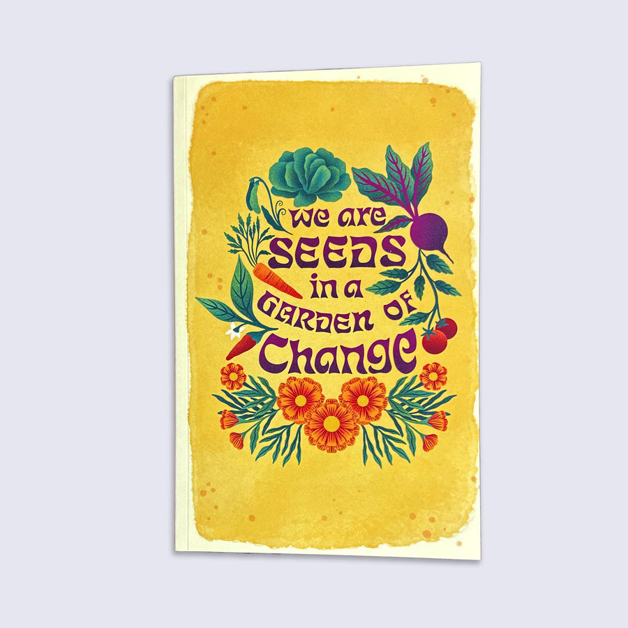 Yellow journal with colorful lettering "we are seeds in a garden of change" surrounded by illustrated vegetables