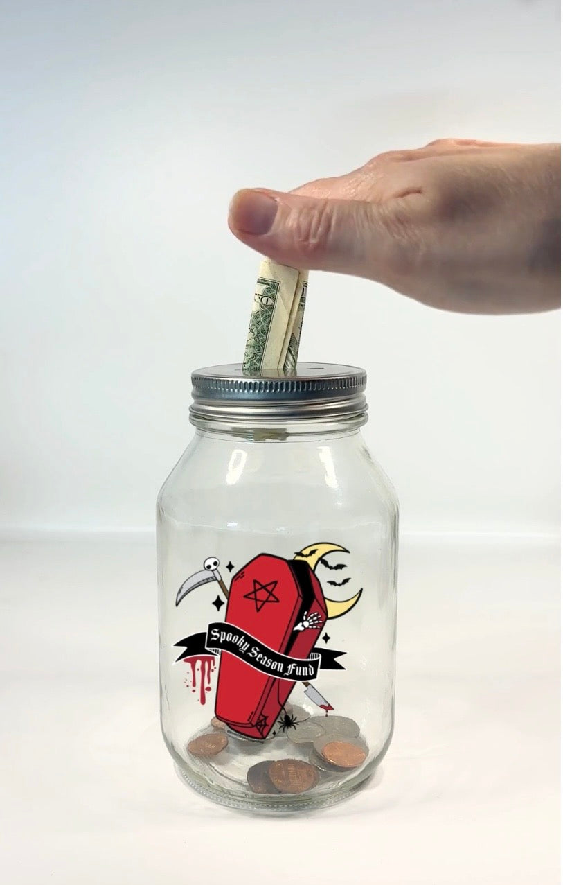 A clear glass mason jar with a silver metal lid, featuring a gothic coffin graphic, with dripping blood, moon, scythe, bats, pentagram, spider, and a moon with the text &