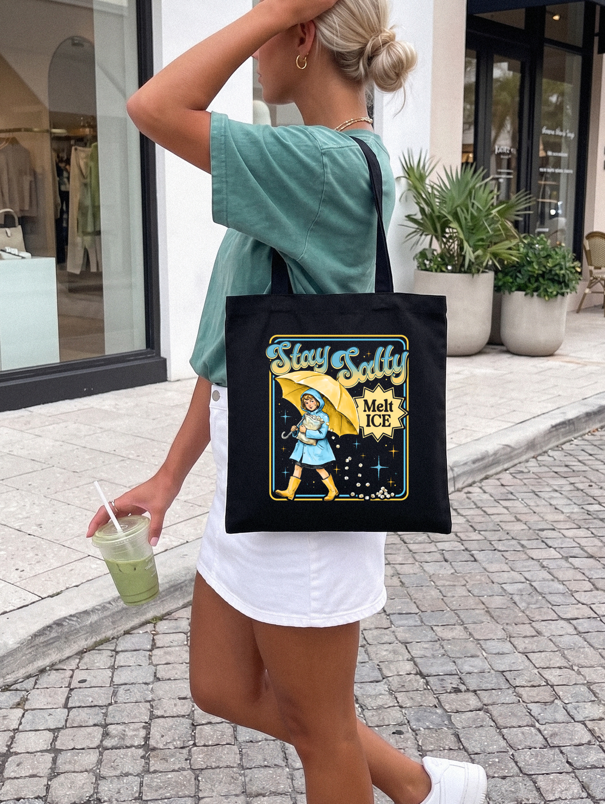 Person holding a tote bag with a graphic design outdoors reads stay salty melt ice