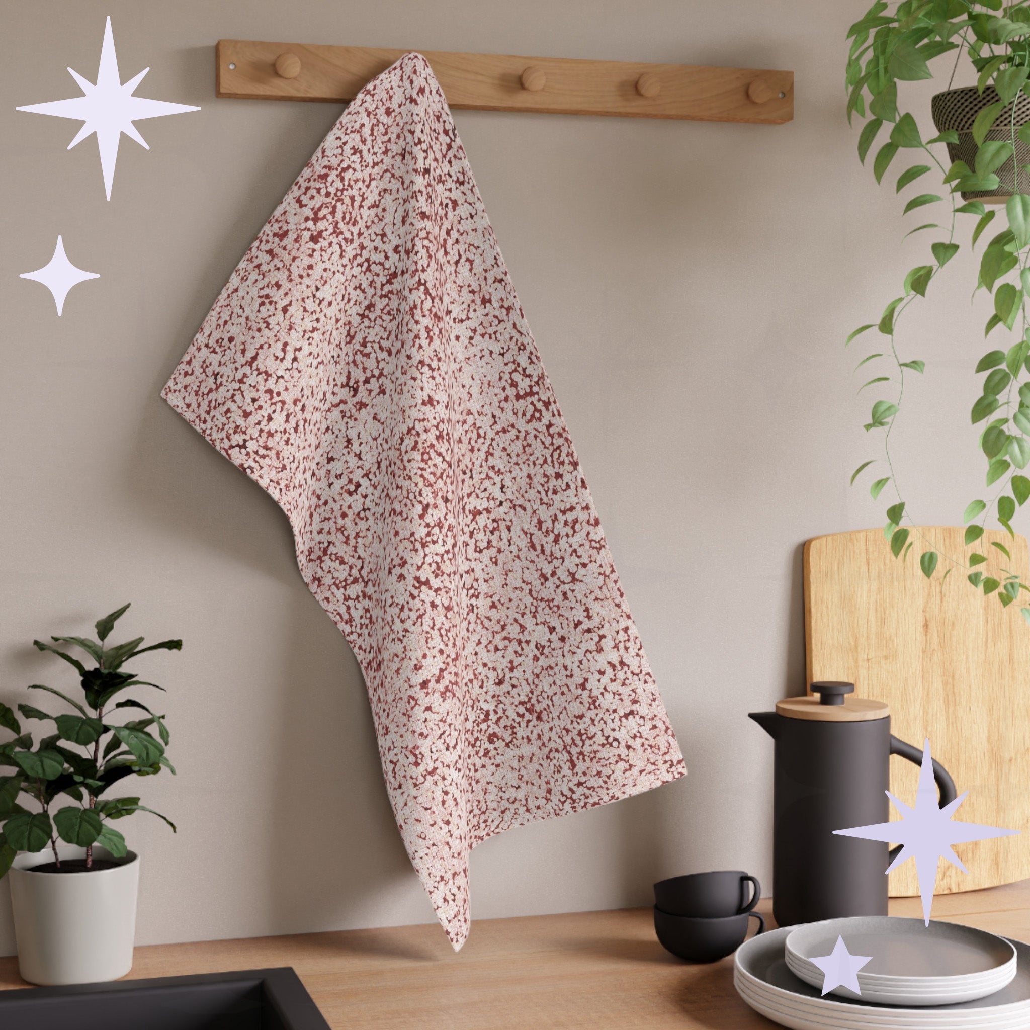 Terracotta red terrazzo kitchen towel hanging from wooden peg rail in neutral kitchen setting with houseplants, stacked plates, and matte black coffee equipment