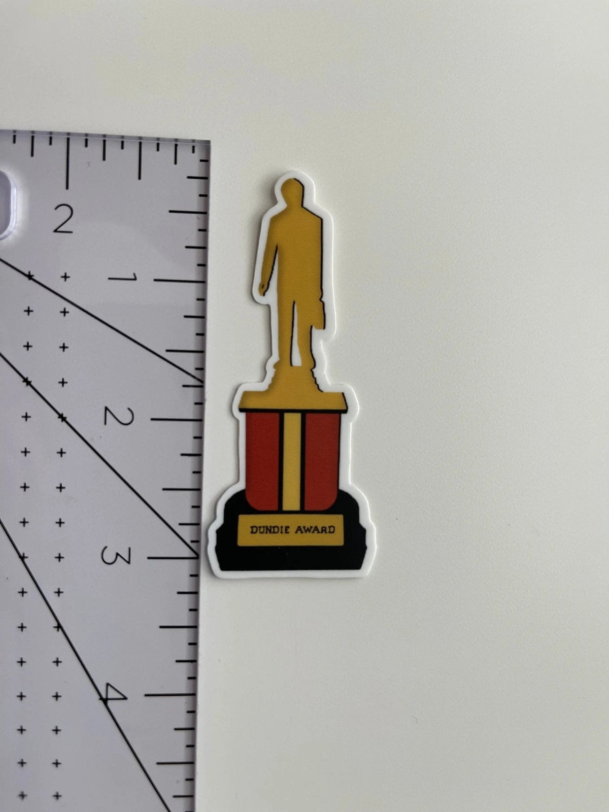 The Office Dundie Award sticker flat lay — funny office humor laptop sticker and coworker gift by indie artist MangoIllustrated