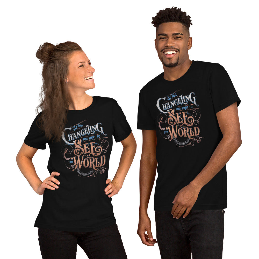 Two models standing side by side in playful poses. One white woman, hands on hips, with half her brunette hair in a bun, and the other half draping past her shoulders. On the right is a tall black man with a goatee. They are both wearing the Unisex Tee with “Be the Changeling you want to see in the world” in silver, bronze and blue lettering surrounded by intricate decals
