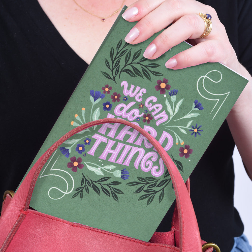 A flat lay notebook with a green cover featuring a floral pattern and the phrase &