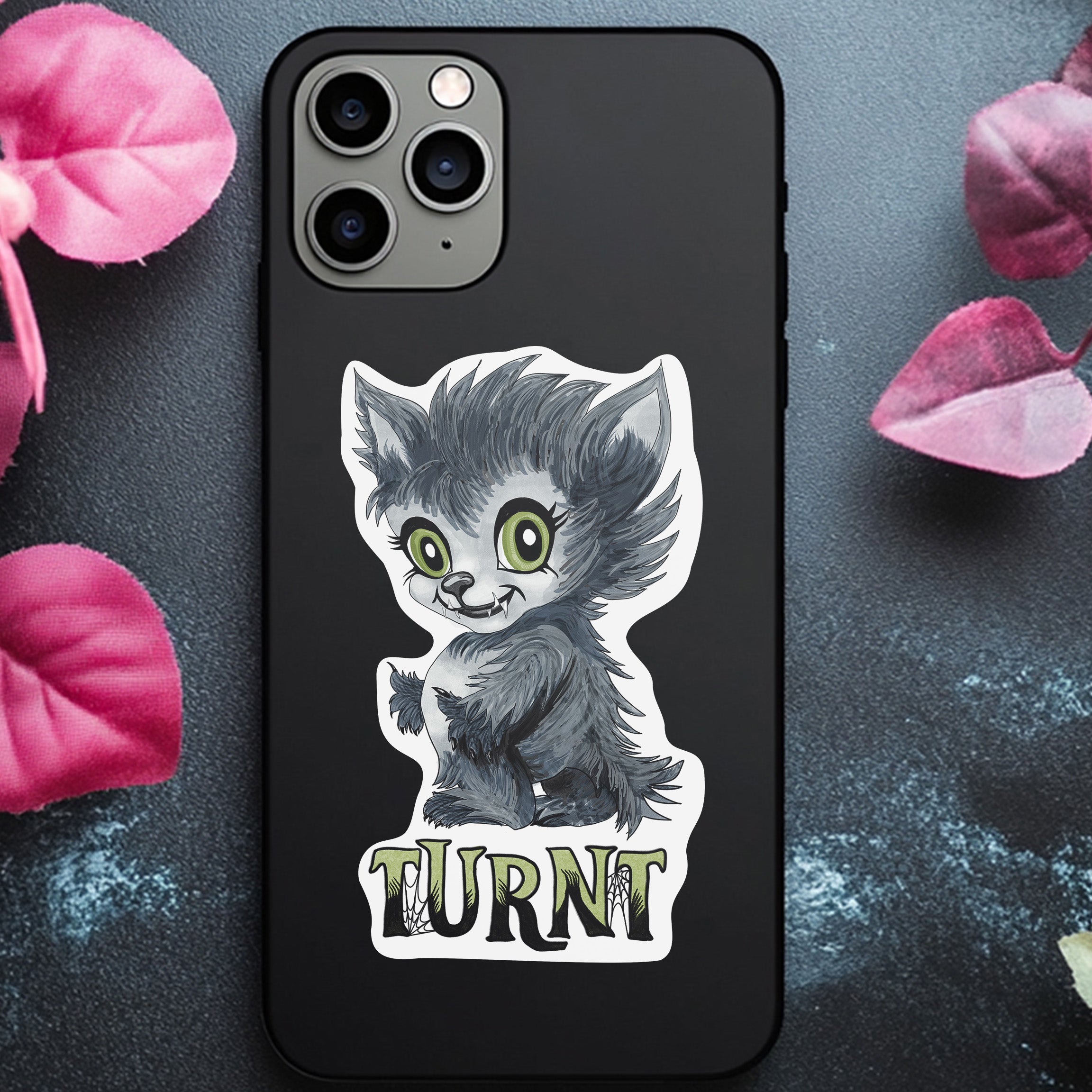Turnt werewolf sticker applied to the back of a black phone case among pink petals