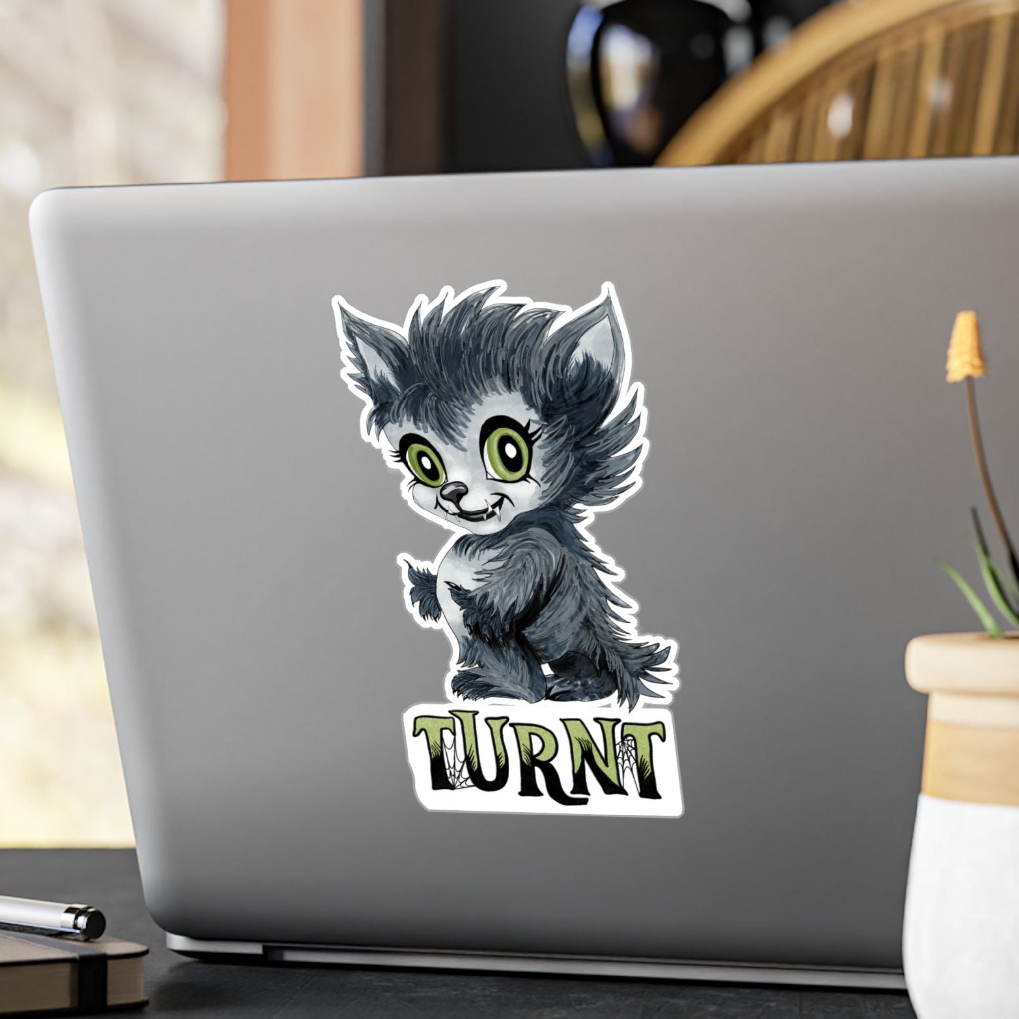 Large chibi werewolf sticker with green eyes and TURNT lettering on the back of a silver laptop