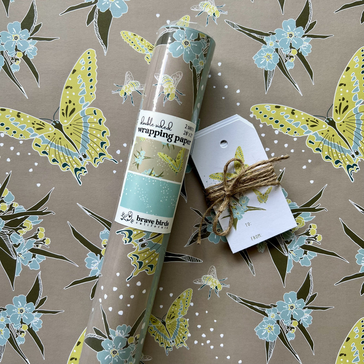 Packaged roll of wrapping paper sitting on a flat sheet of the paper showing the full pattern, shown with coordinating gift tags