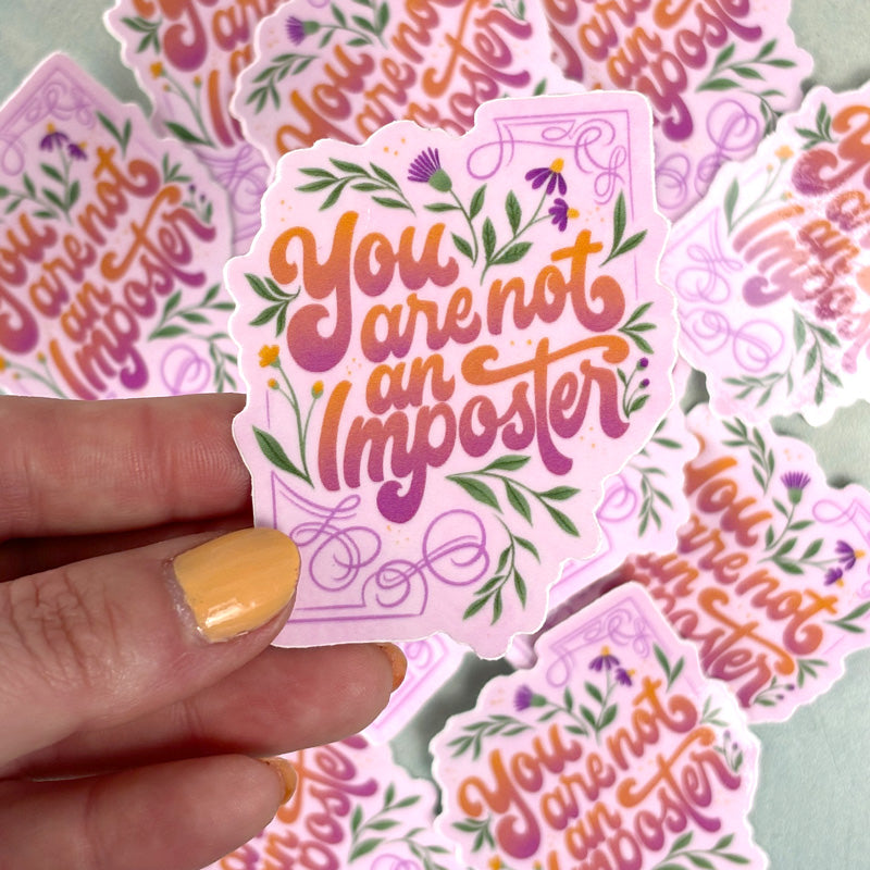 handing holding A sticker with a floral design and the lettering &